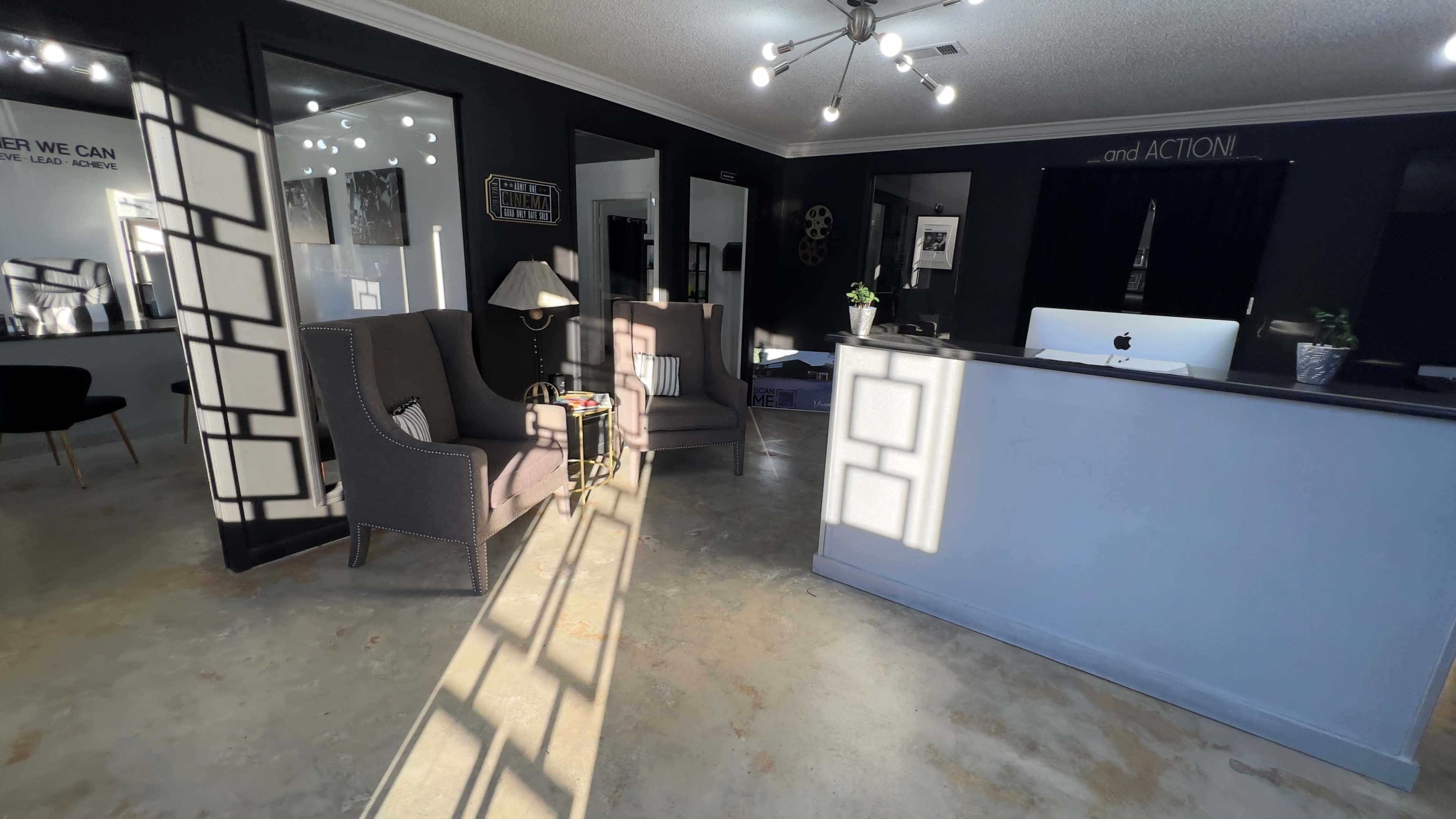 A modern interior space with two armchairs facing a reception desk, illuminated by shadows from window panes.