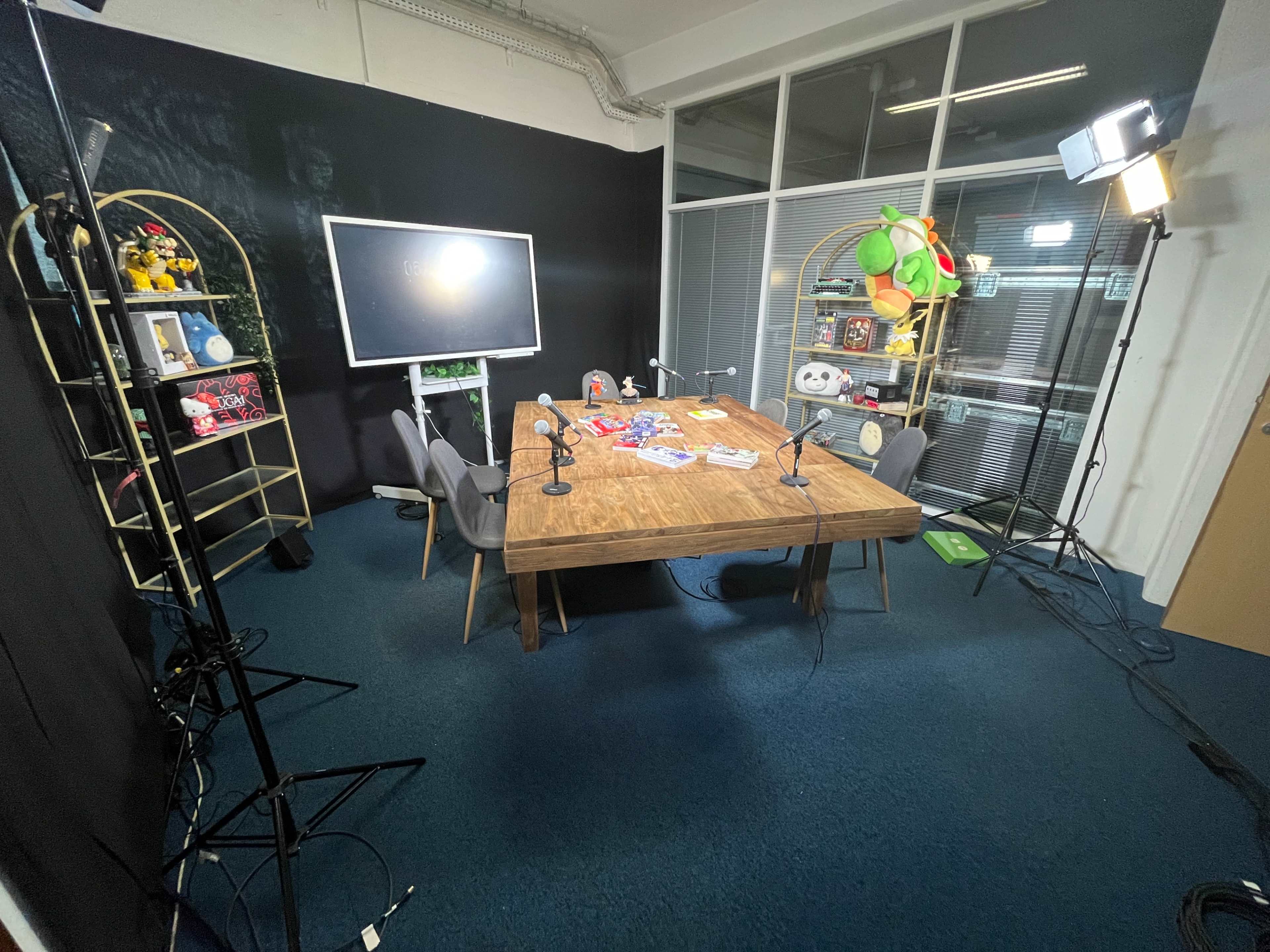 A recording studio setup with a wooden table, chairs, microphones, and various props on a dark backdrop.