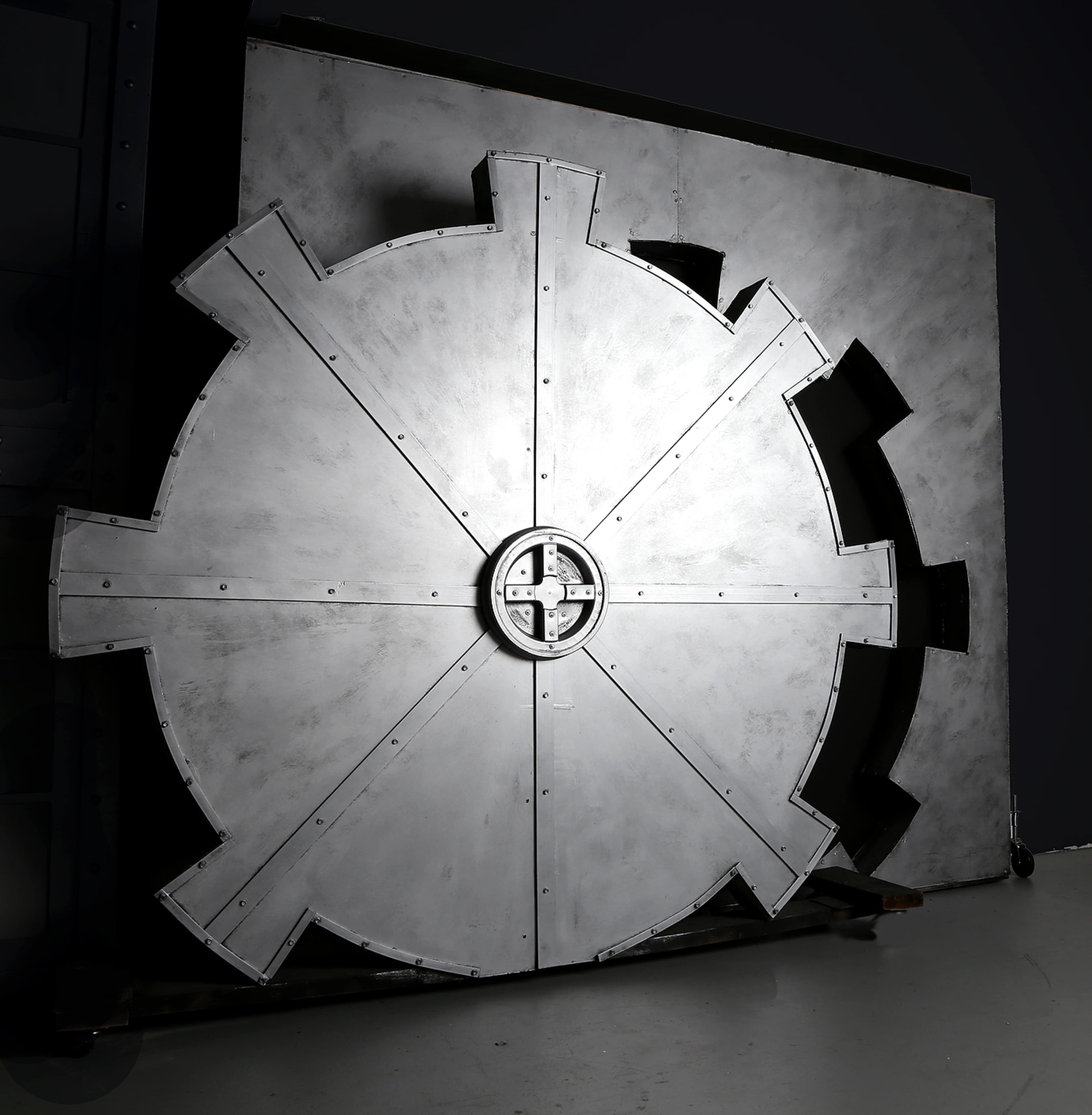 A large, circular metallic vault door with a symmetrical design, set against a dark background.