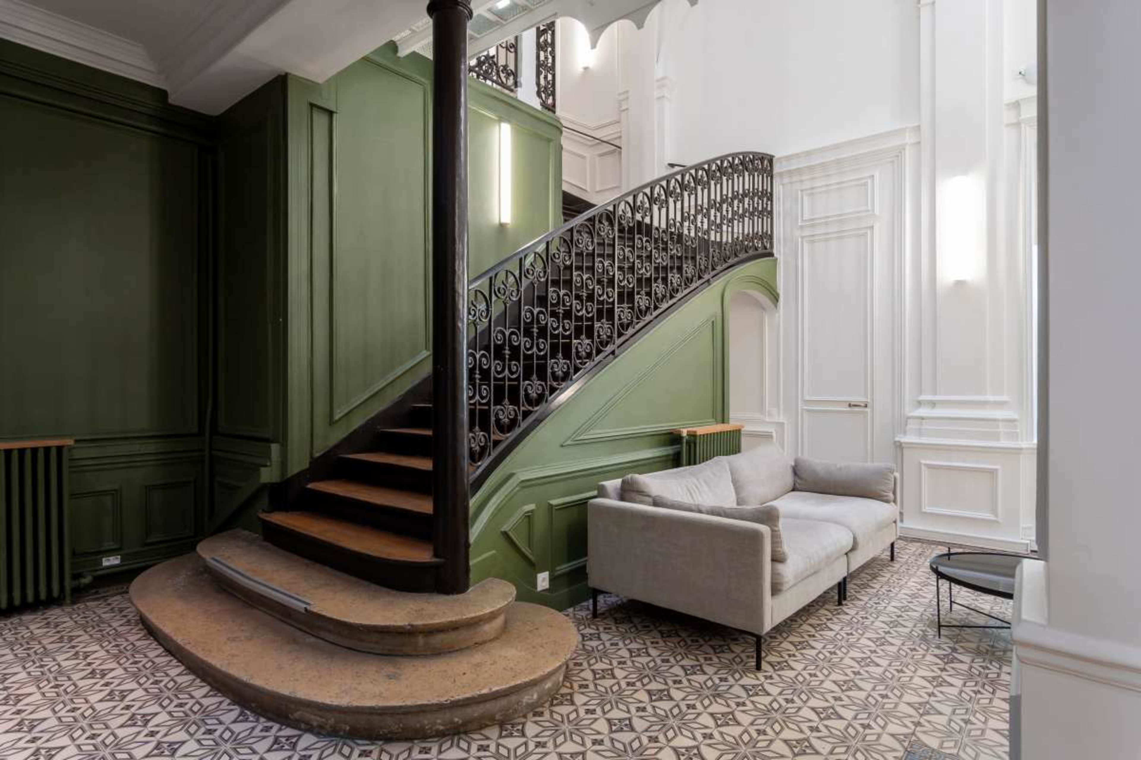 The image depicts a stylish interior featuring a curved staircase with ornate railing, a light-colored sofa, and patterned tiled flooring.