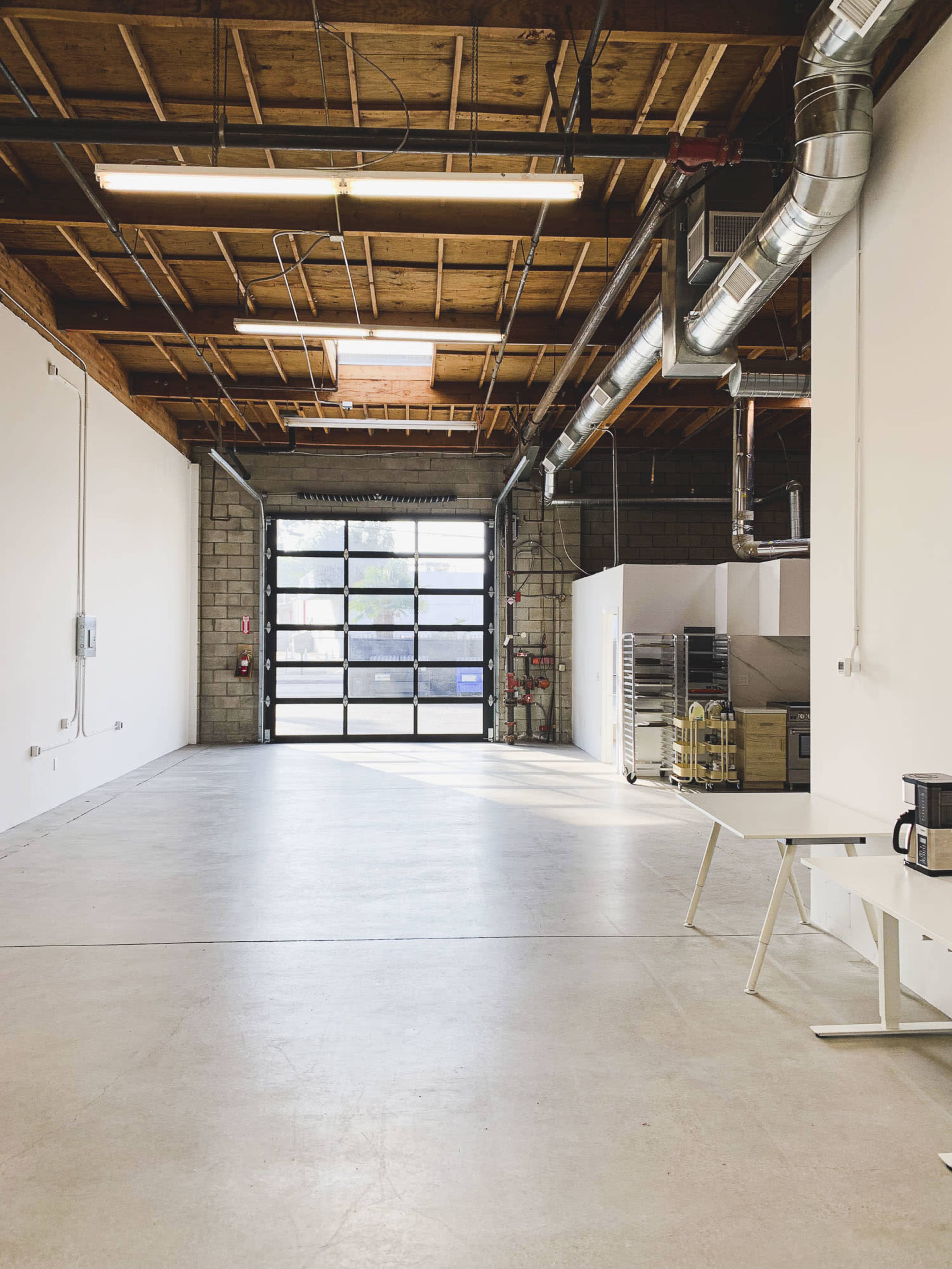 A large, empty warehouse space with a roll-up glass door and exposed wooden beams in the ceiling.