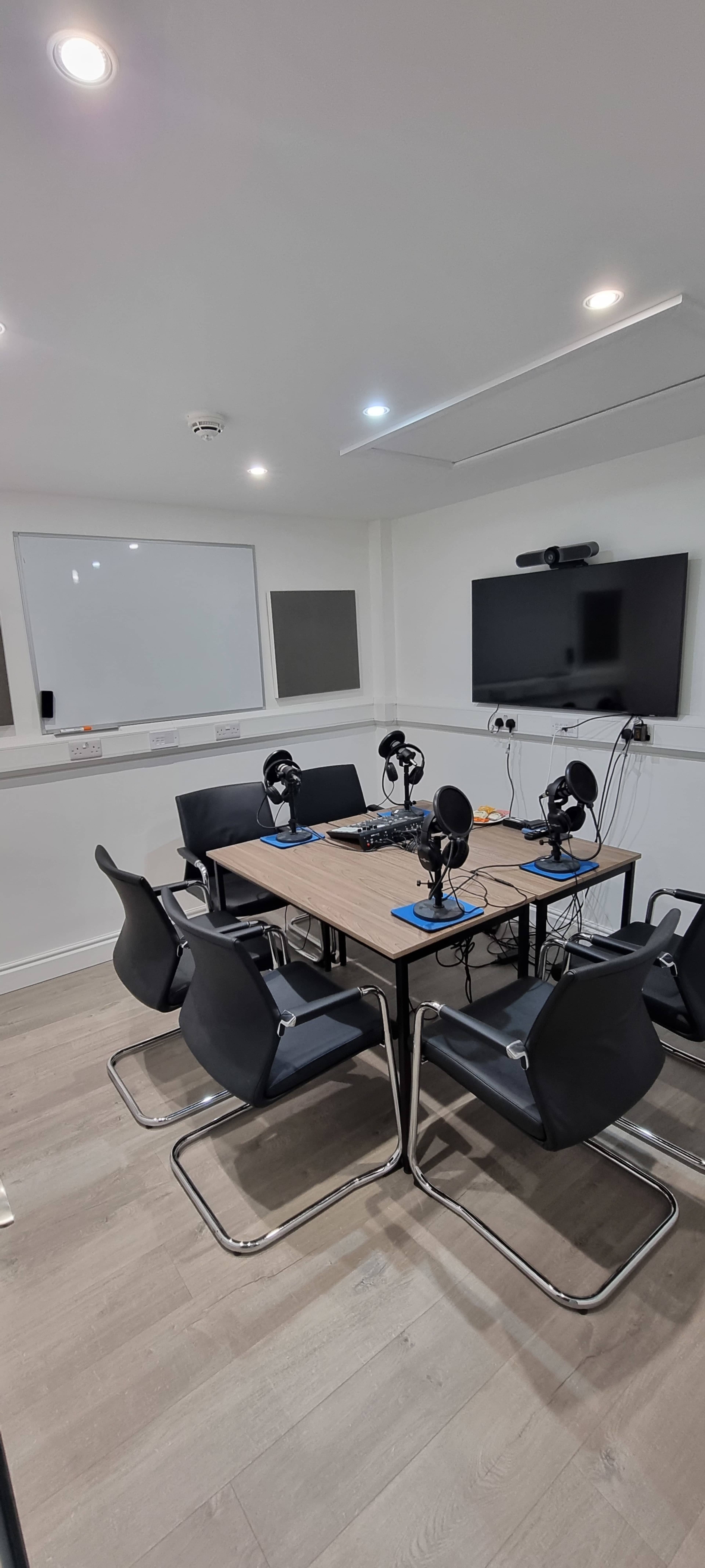 A conference room is set up with a table and chairs, equipped with microphones and audio equipment for recording or broadcasting.