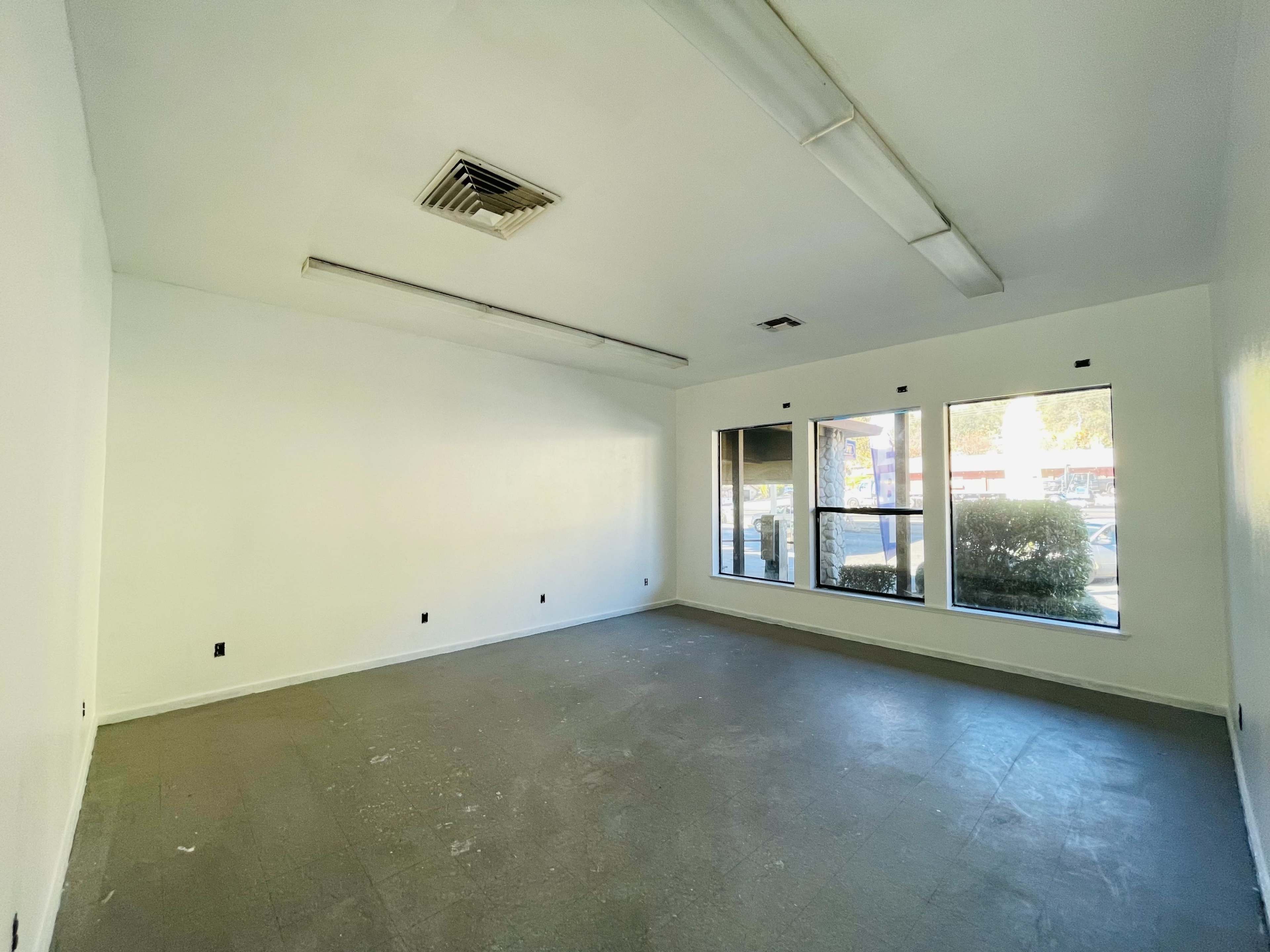 An empty room with white walls and large windows overlooking a sidewalk.