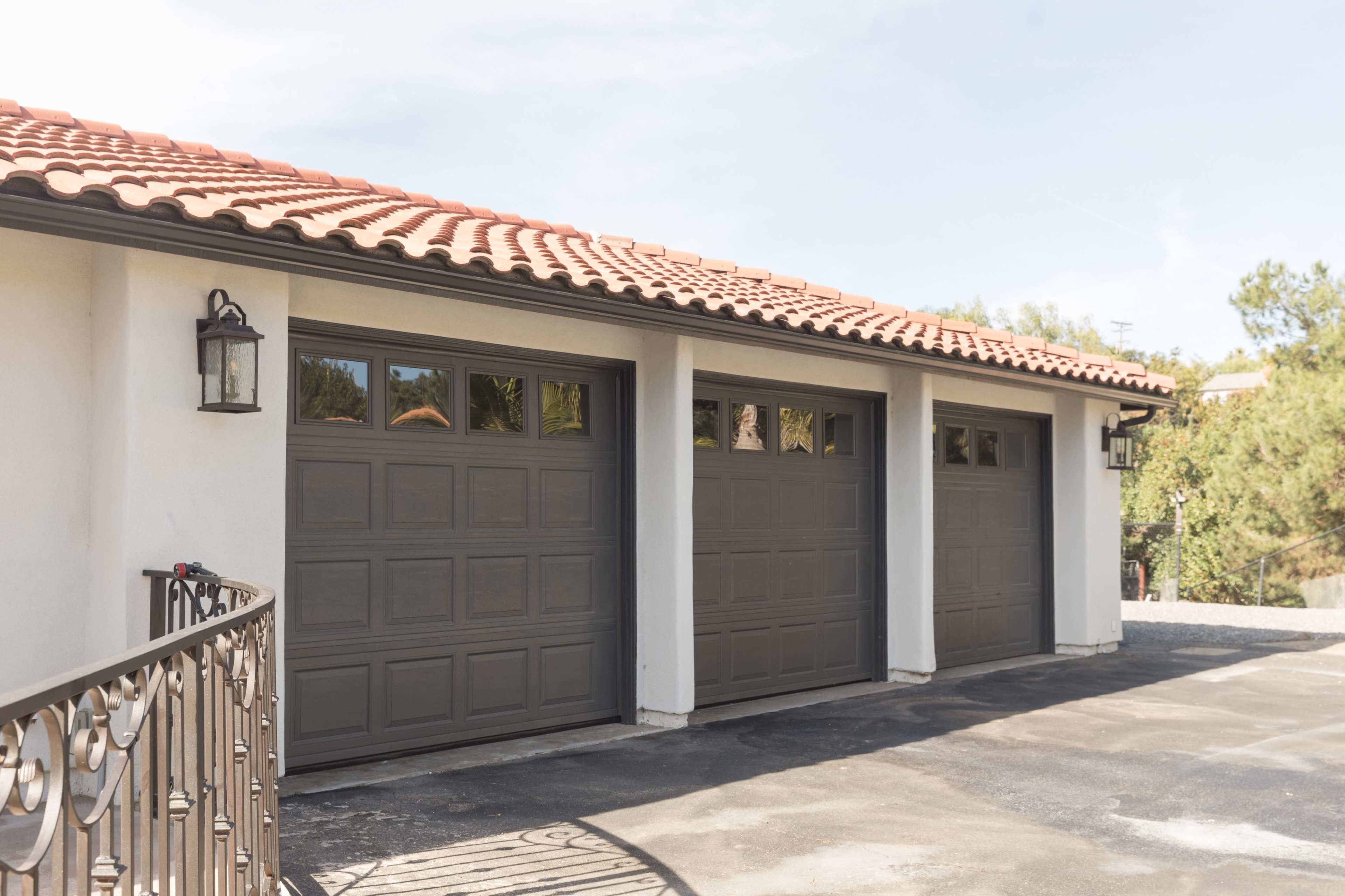 The image shows a residential driveway with three gray garage doors beneath a tile roof.