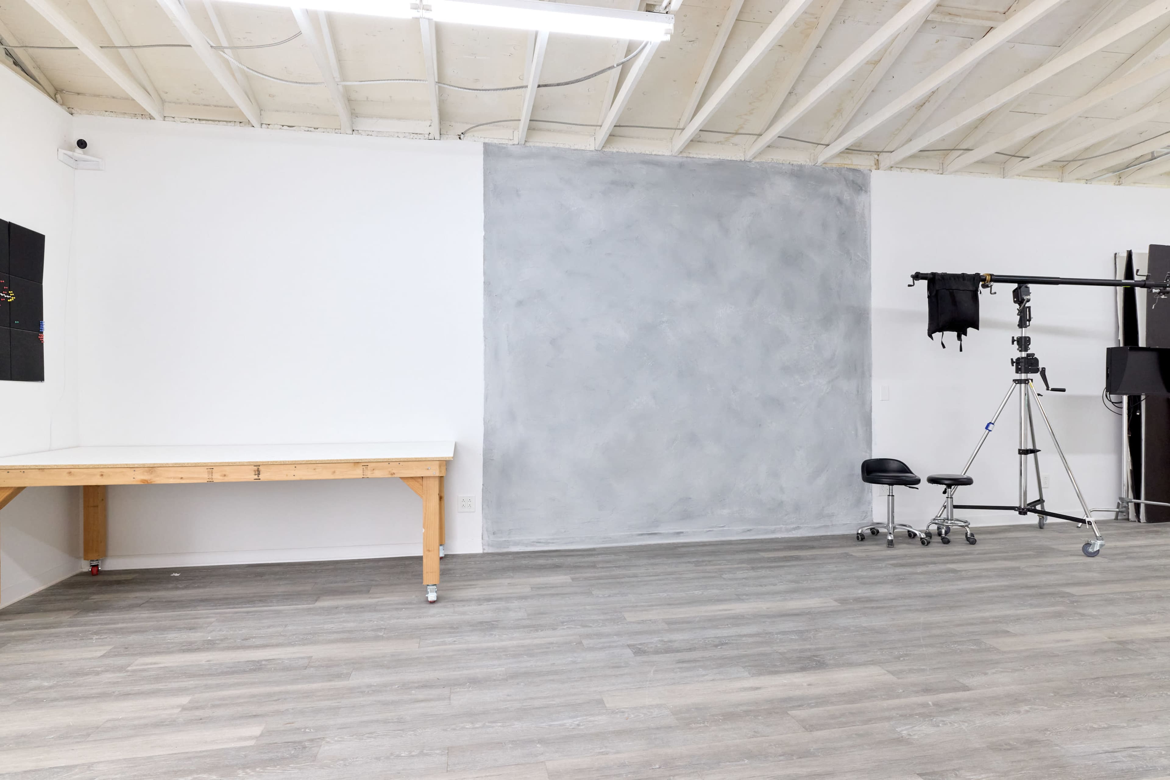 A spacious studio with a wooden table, a gray wall, and photography equipment set up on wheels.