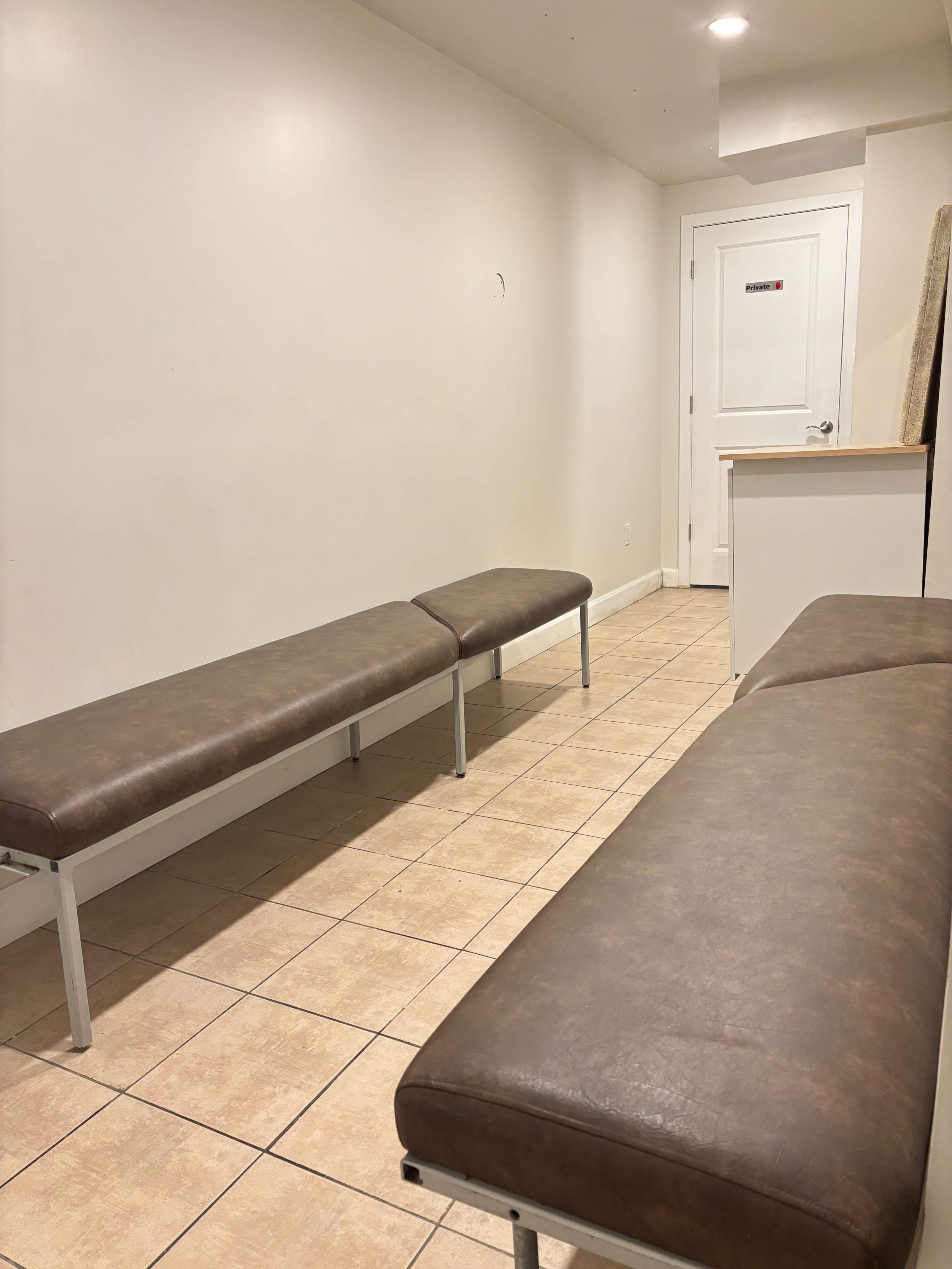 The image shows a narrow waiting area with two brown benches and a door at the far end.