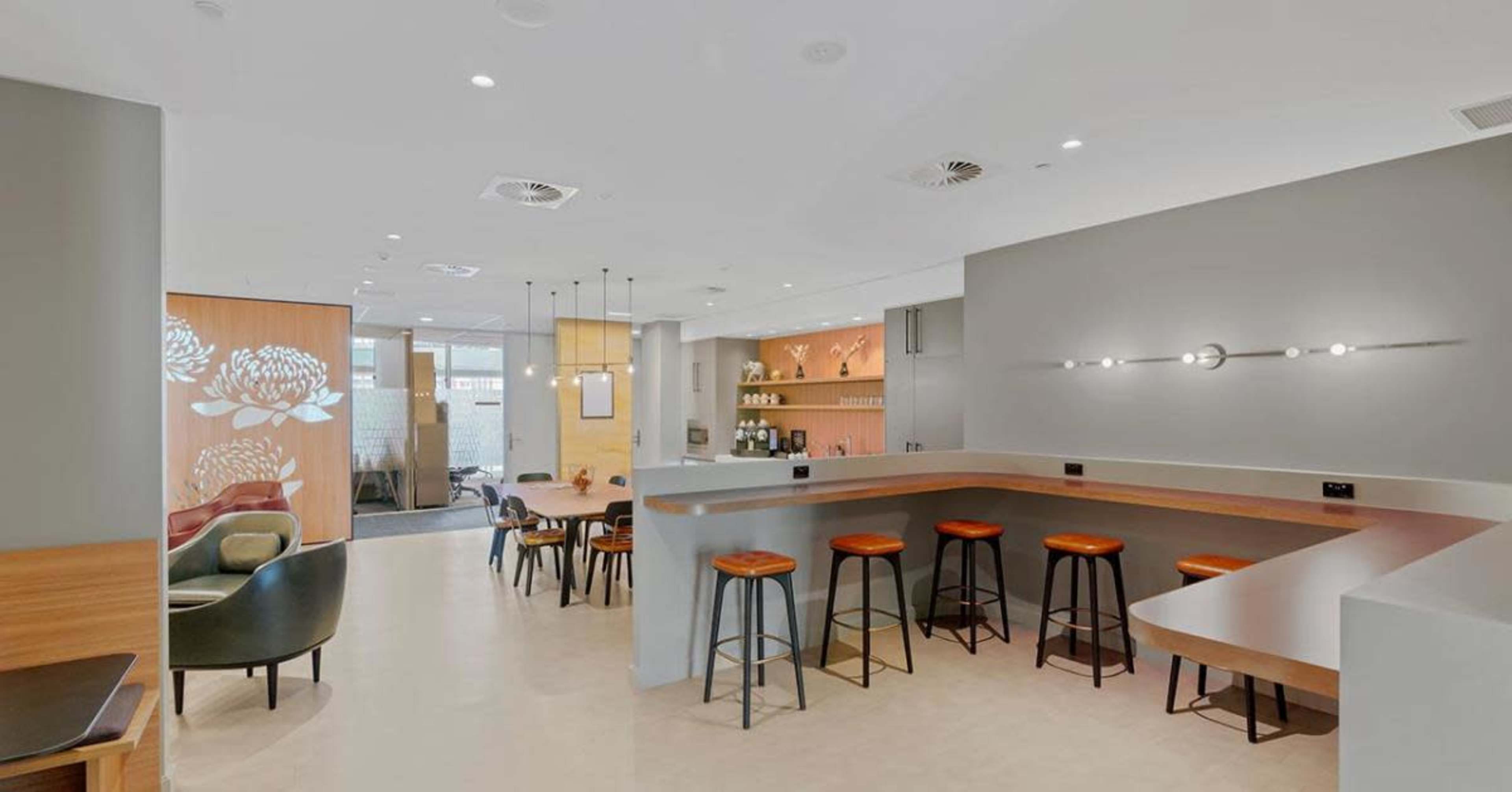 A spacious, modern café features a minimalist design with a wooden bar, high stools, and a variety of seating options.