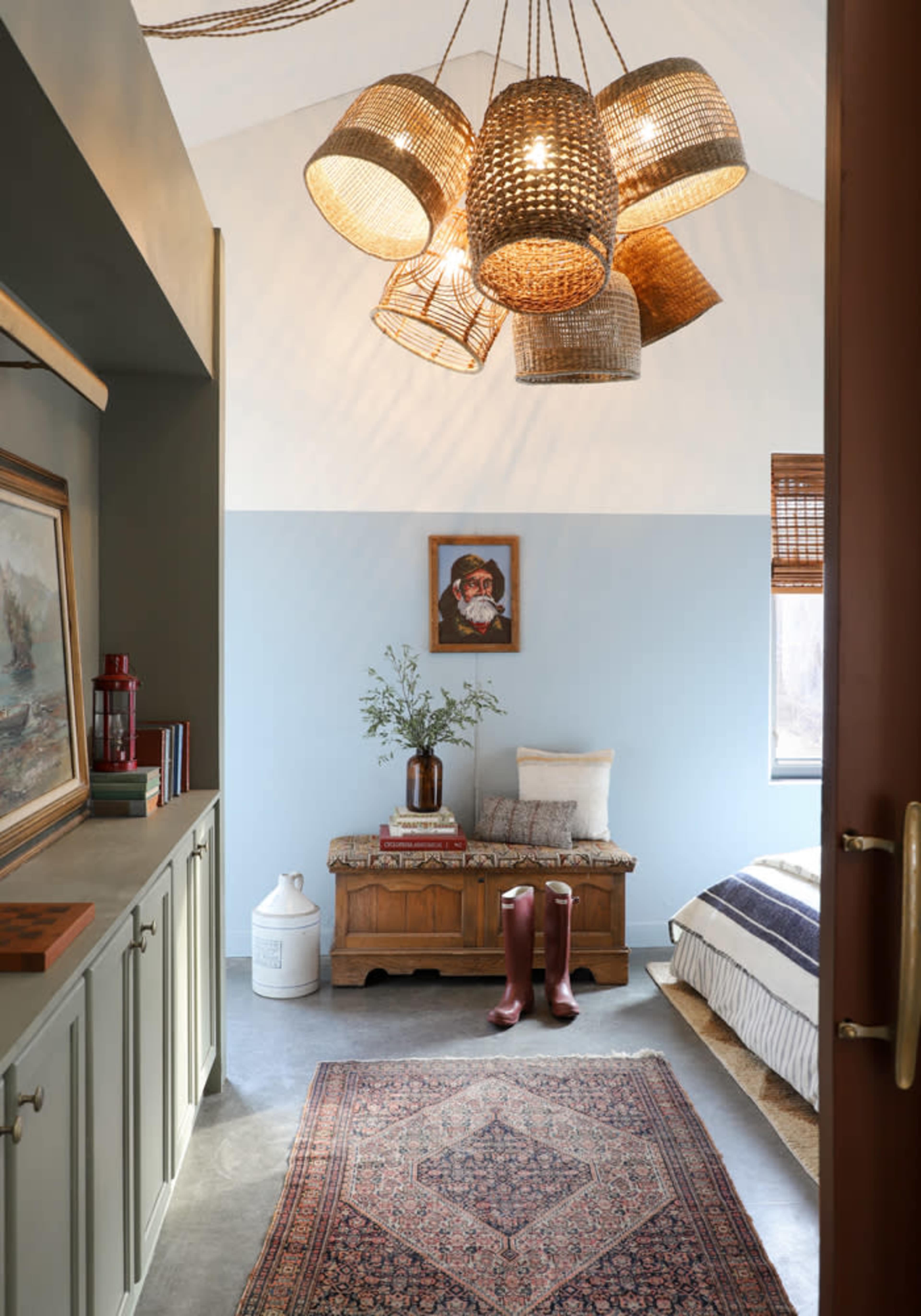 A warmly lit bedroom features a bench, a vase of flowers, and hanging woven light fixtures, with a patterned rug on the floor.