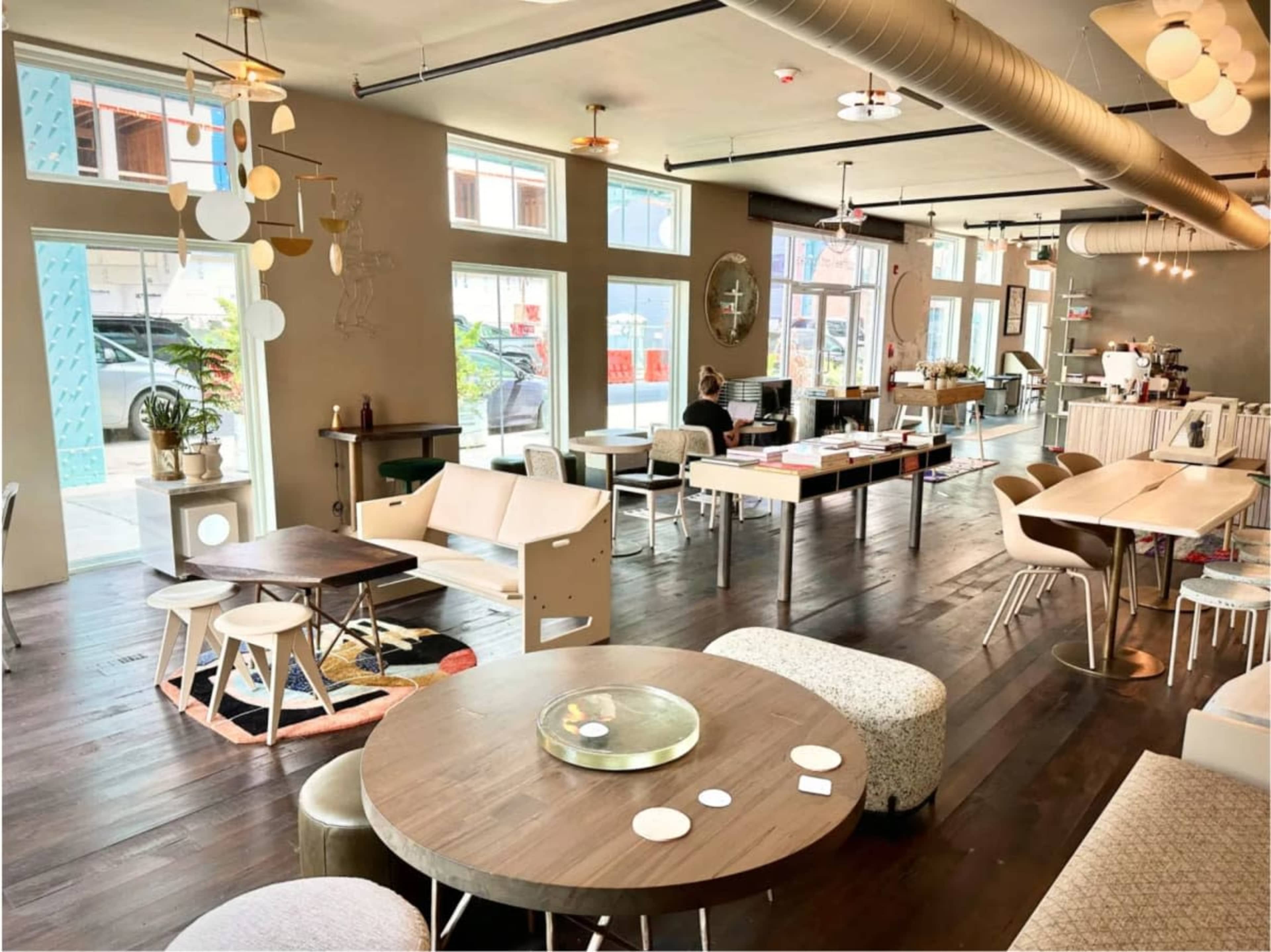 The image shows a modern café interior with various seating arrangements, large windows, and a bright, open layout.
