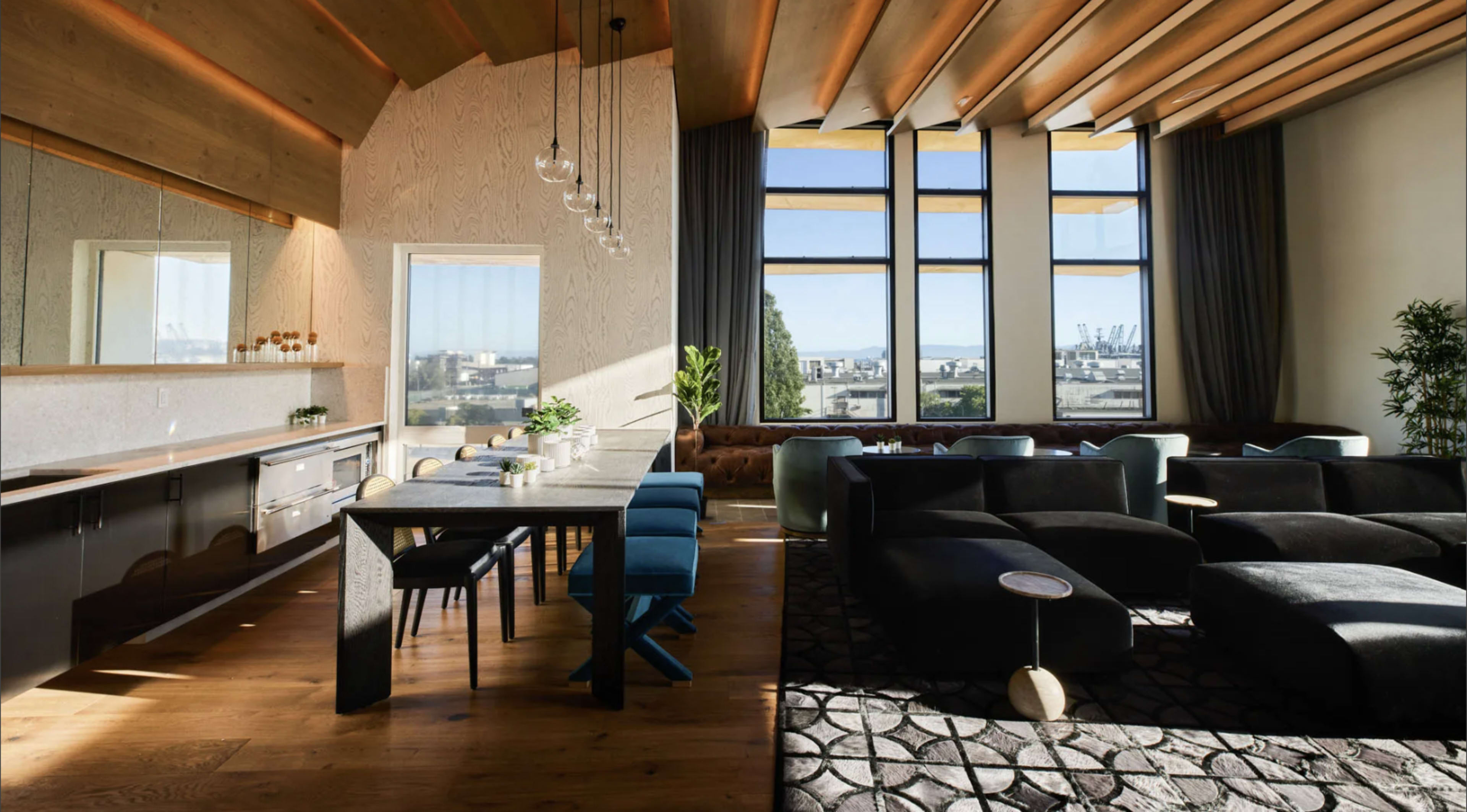 A modern living space features a dining table with blue chairs, a sleek kitchen area, and large windows that overlook a cityscape.