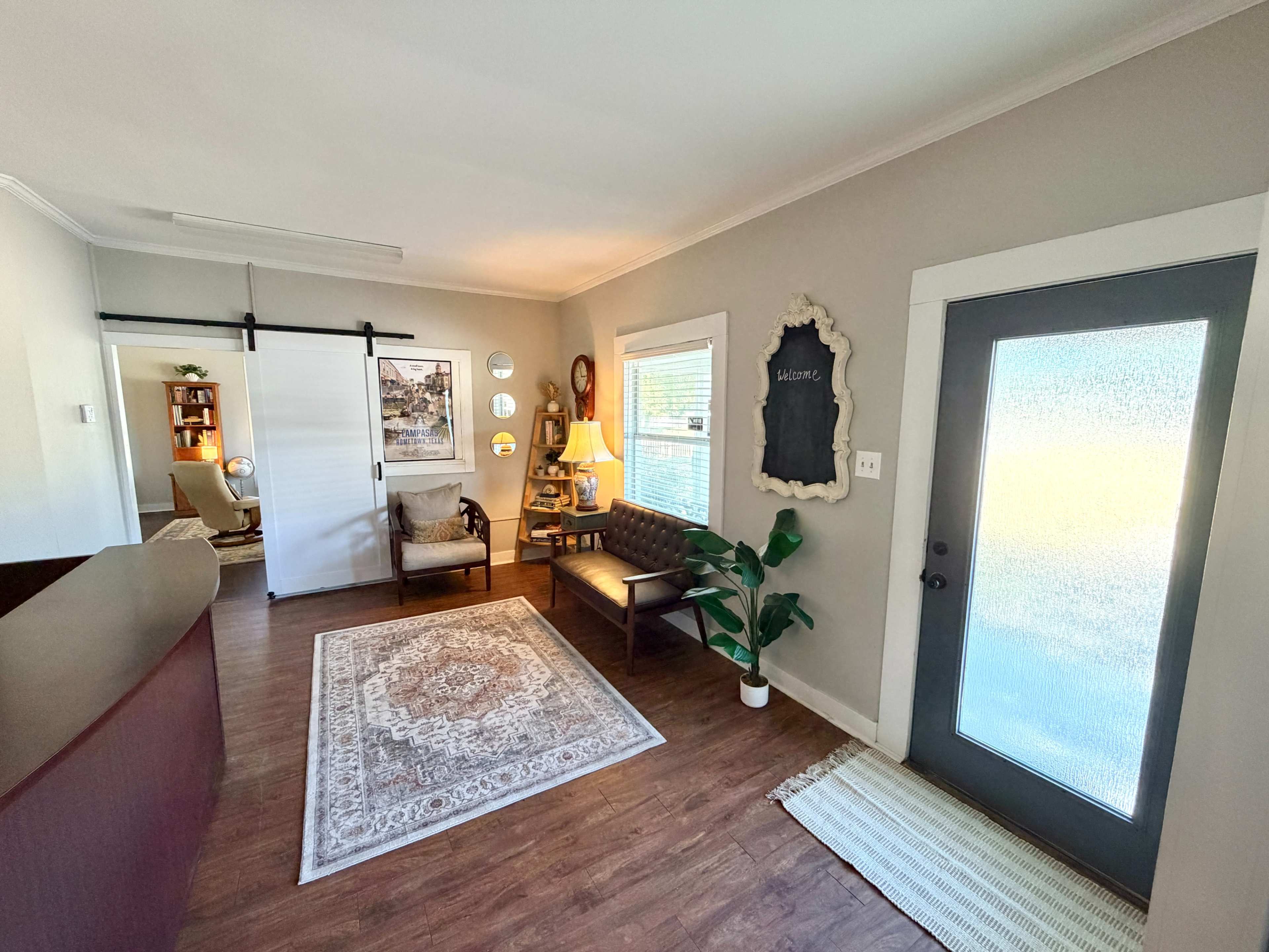The image shows a cozy entryway with a seating area, a decorative rug, a chalkboard, and a front door with a frosted glass panel.