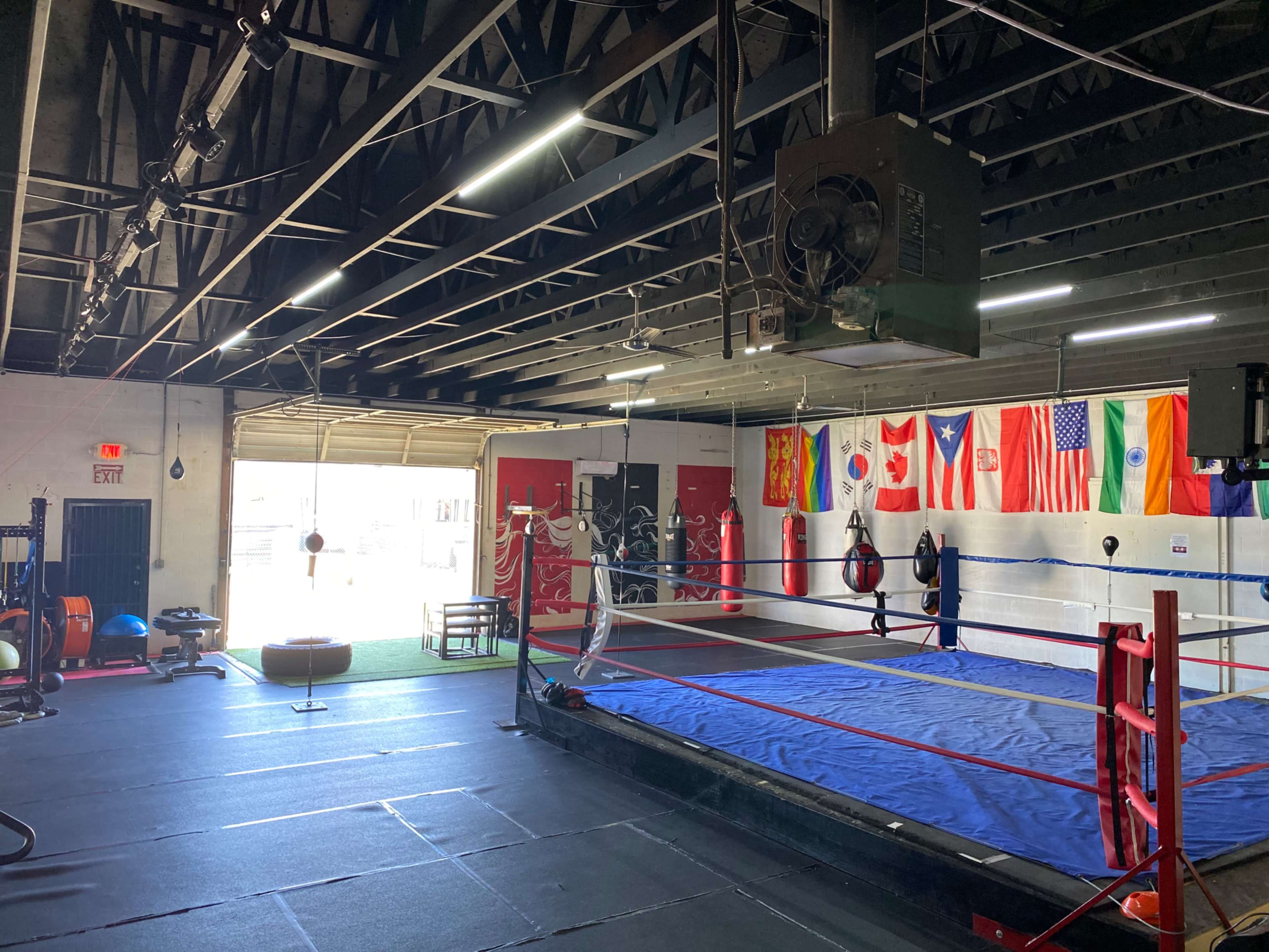 A gym with a boxing ring, exercise equipment, and several flags from different countries hanging on the wall.