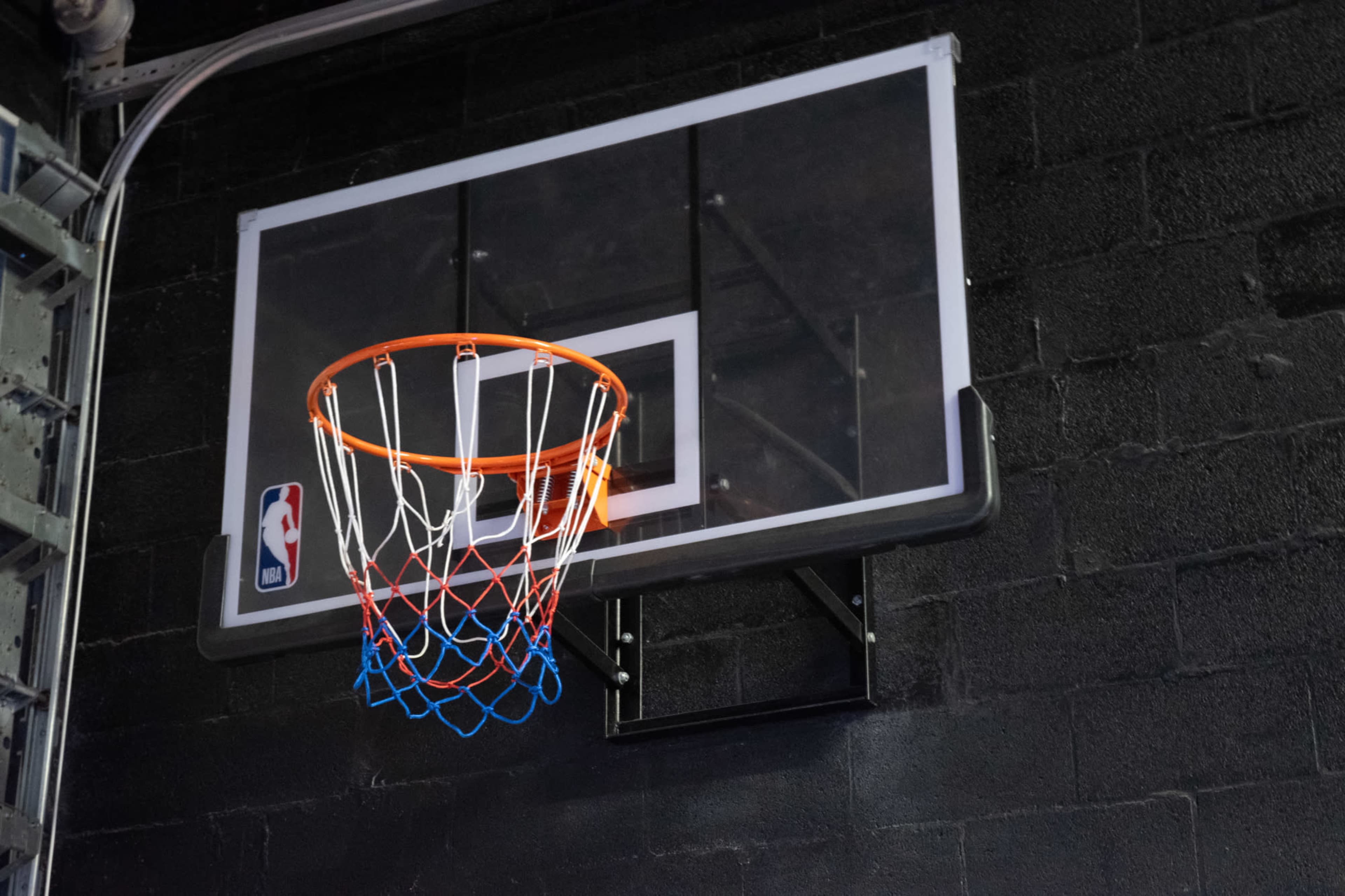 A basketball hoop with a clear backboard and net is mounted on a black wall.
