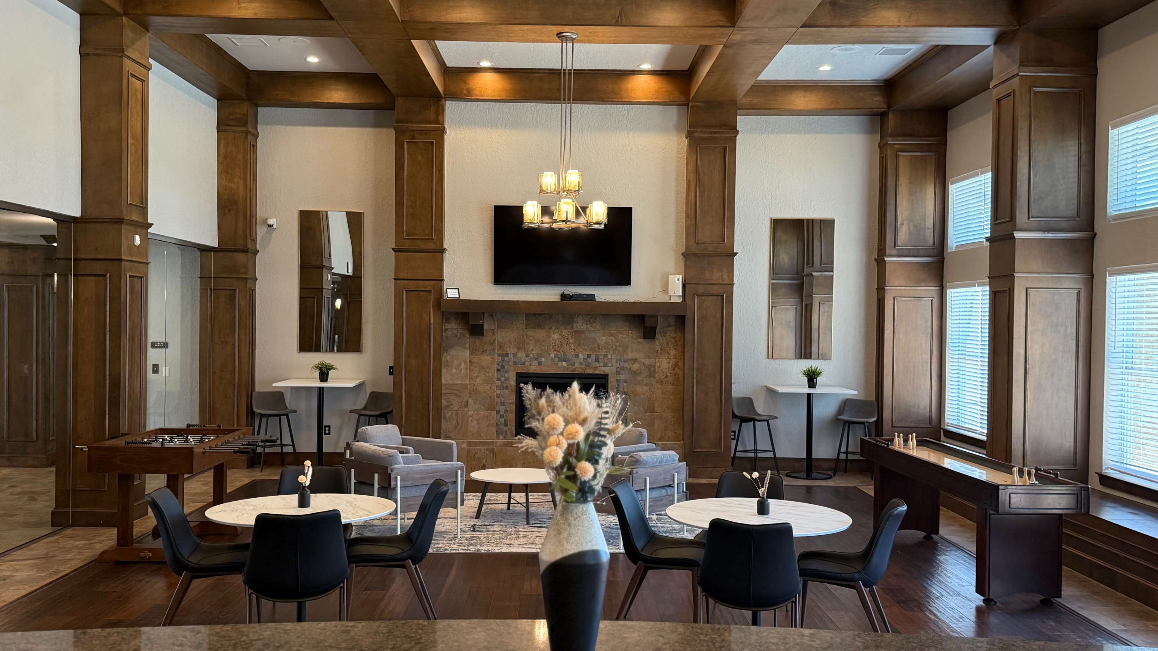 The image shows a spacious lounge area with comfortable seating, a fireplace, and modern decor, illuminated by natural light through large windows.