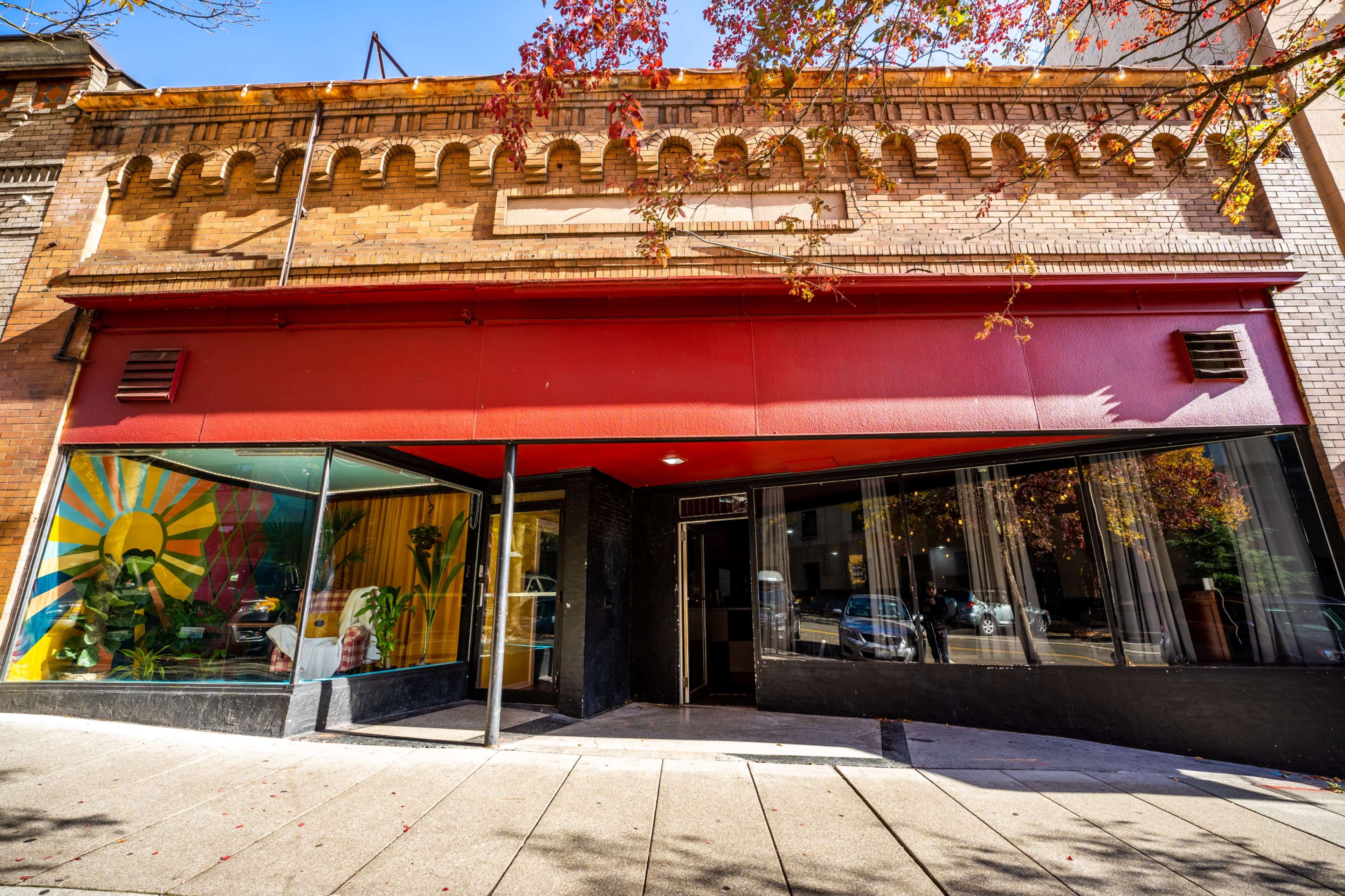 The image shows a storefront featuring a large window display with a colorful mural and a red awning in a brick building.