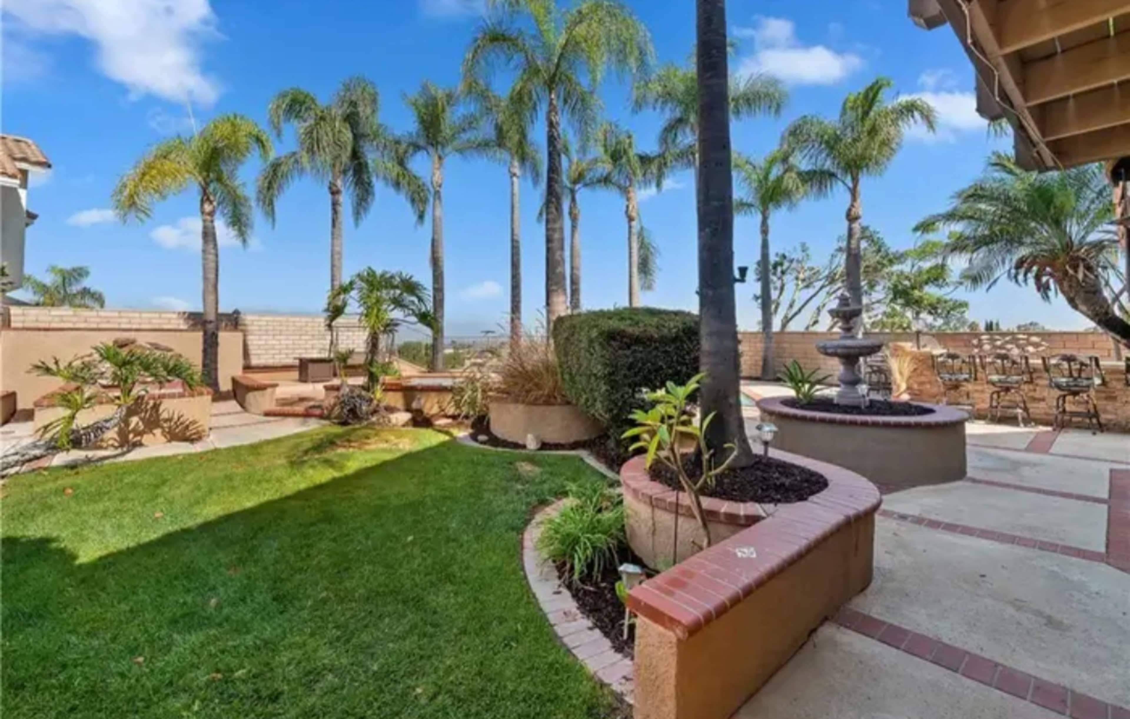 A landscaped yard featuring palm trees, garden beds, and a patio area with seating.