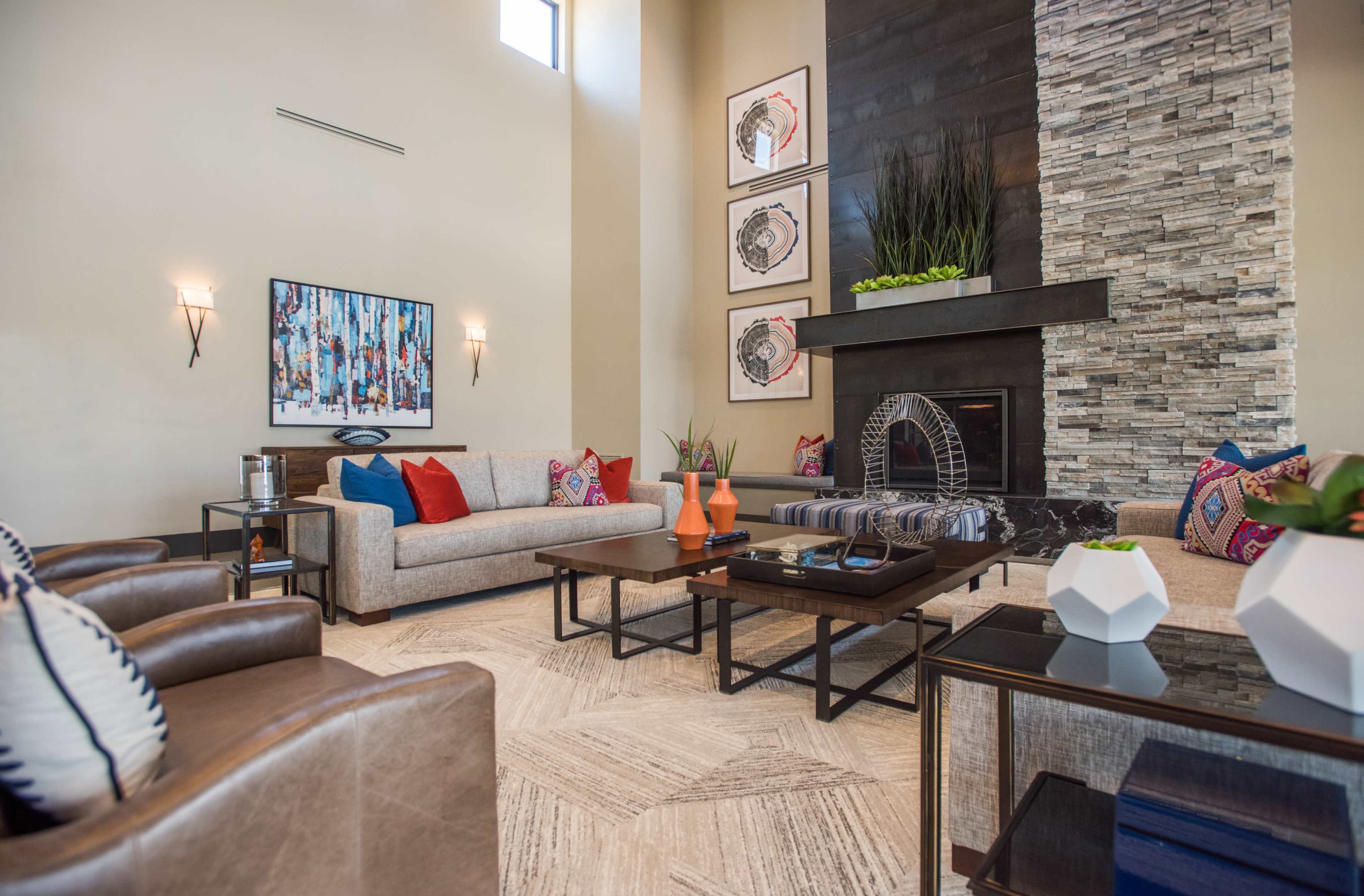 A modern living room with a high ceiling, featuring a stone fireplace and various seating arrangements, including a sofa and leather chairs.
