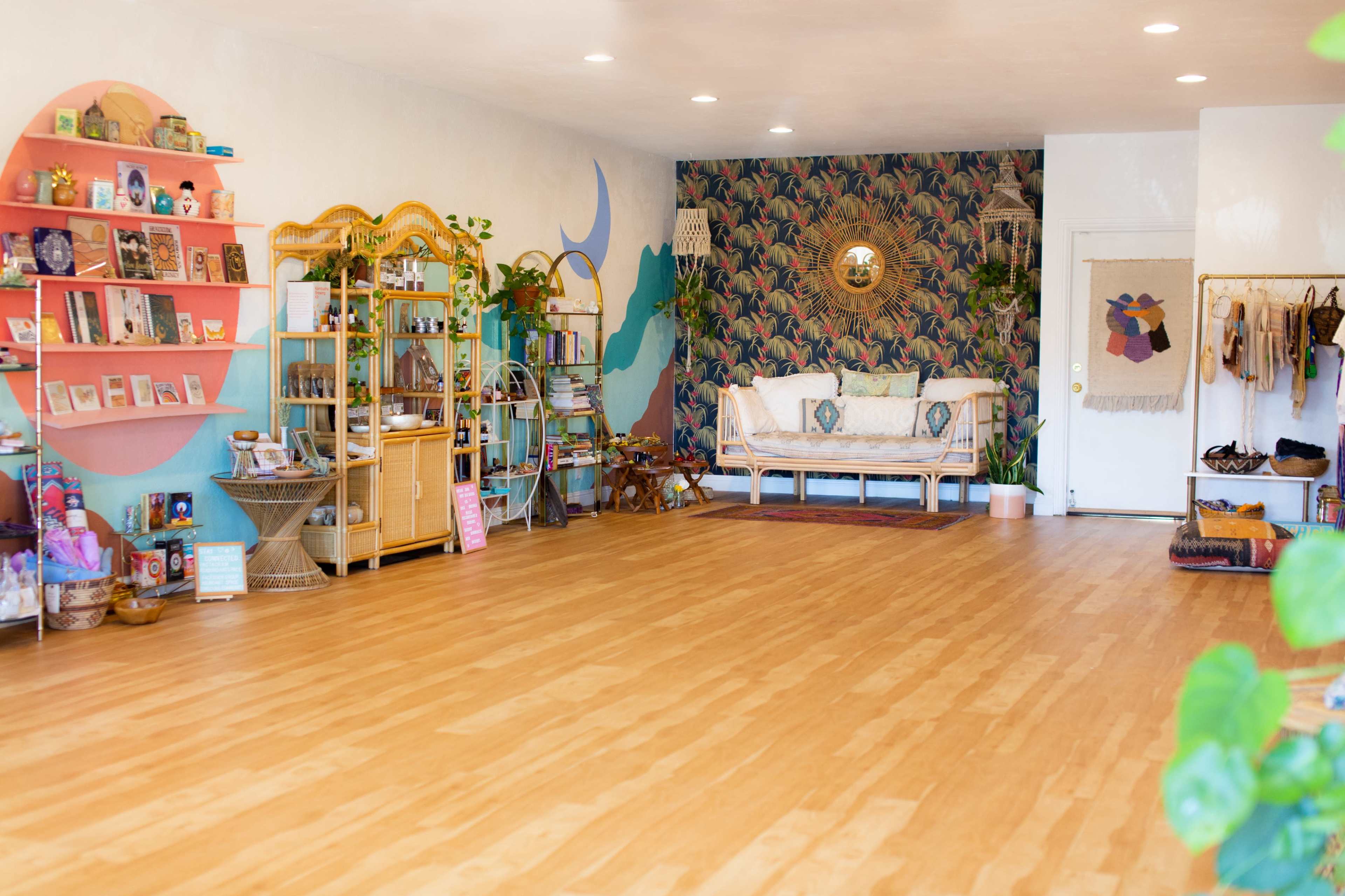 A bright interior space with wooden floors, decorated with bookshelves, plants, and a seating area, all against a colorful patterned wall.