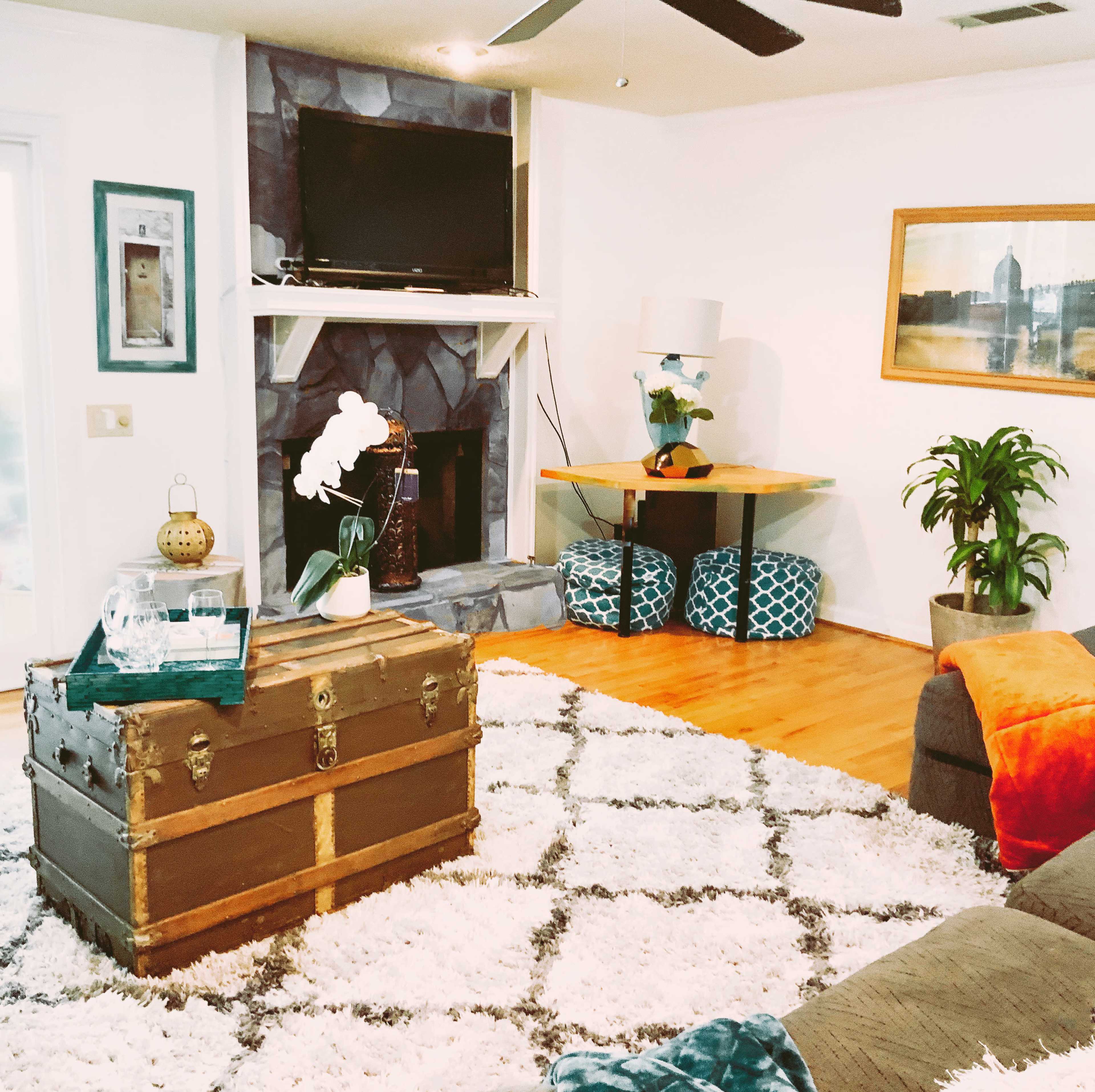 The living room features a fireplace with a mounted TV above it, a wooden coffee table, and a large area rug with geometric patterns.
