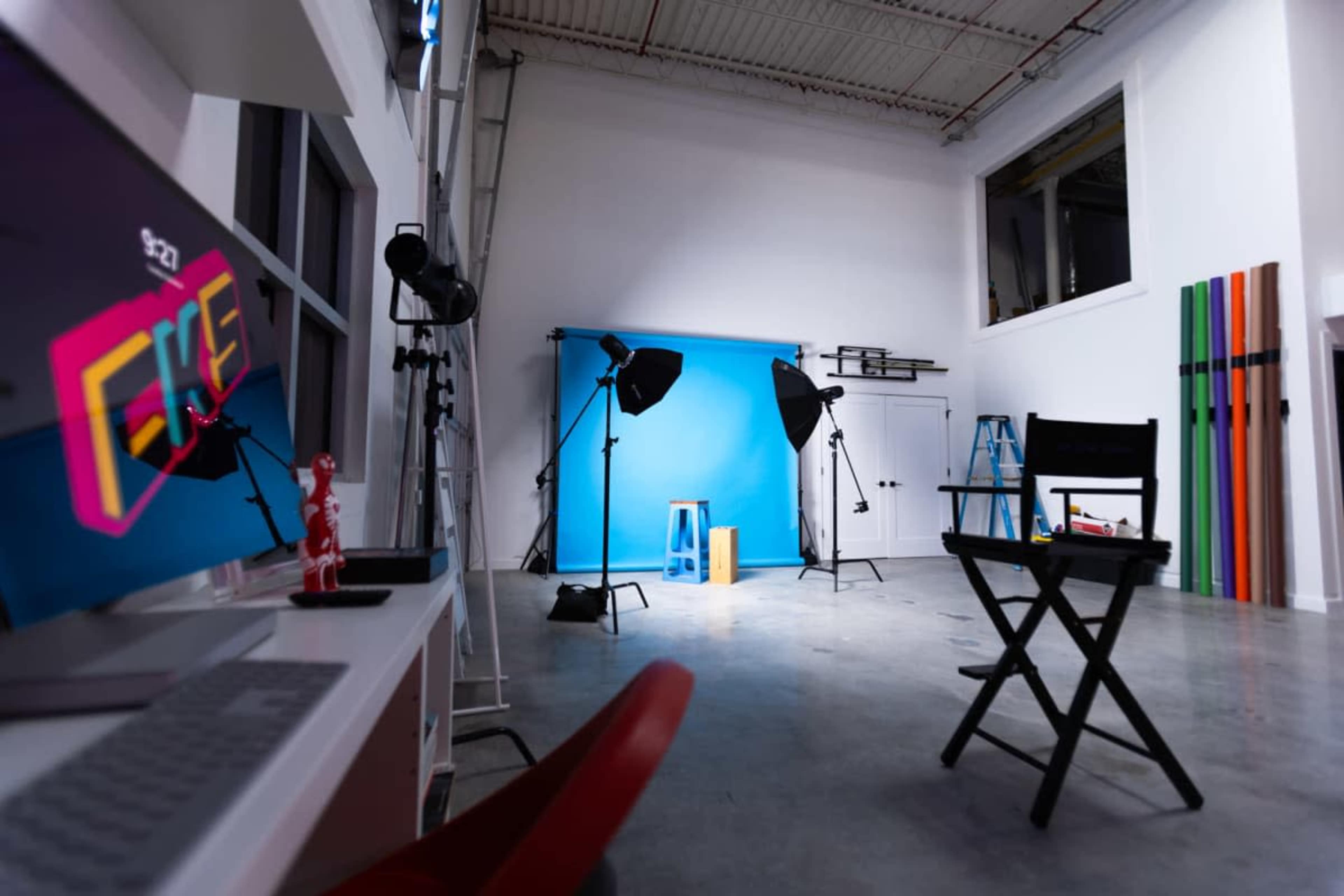 The image shows a photography studio equipped with a blue backdrop, lighting equipment, and a director's chair.