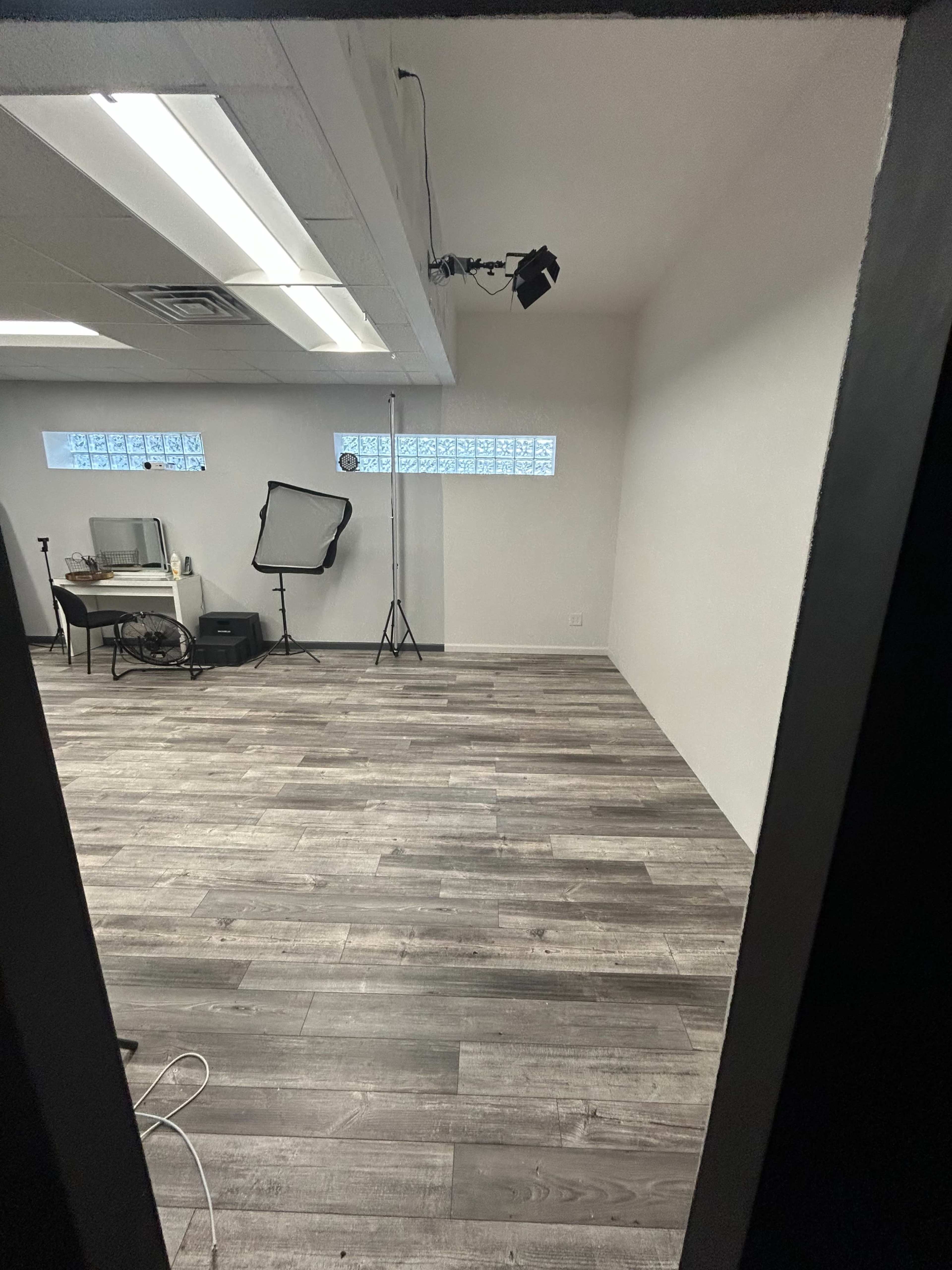 The image shows a minimalist studio space with wooden flooring, a few pieces of equipment, and a bright, well-lit area through a doorway.