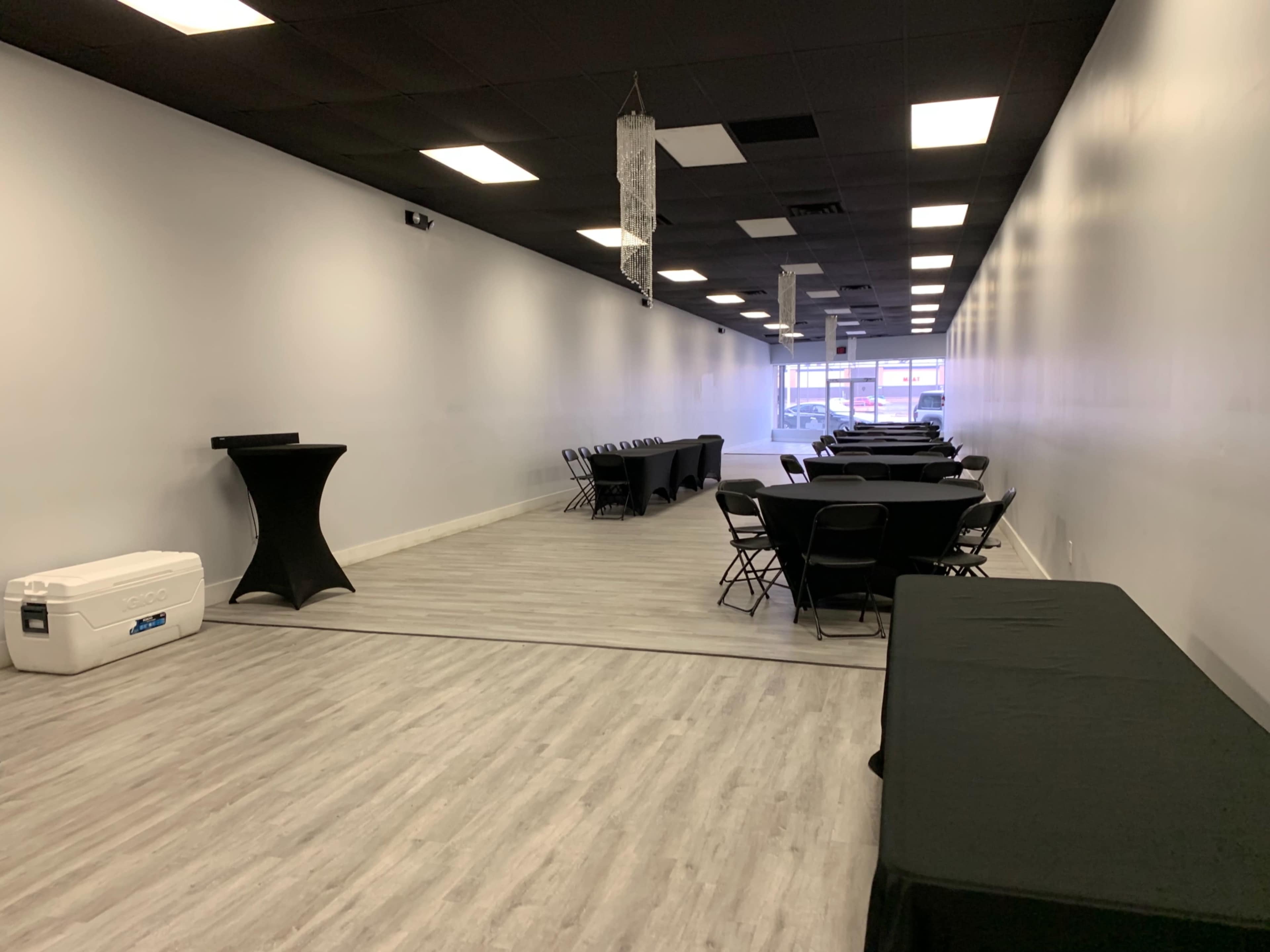 An empty room features several tables covered with black cloths and folding chairs arranged along the sides.