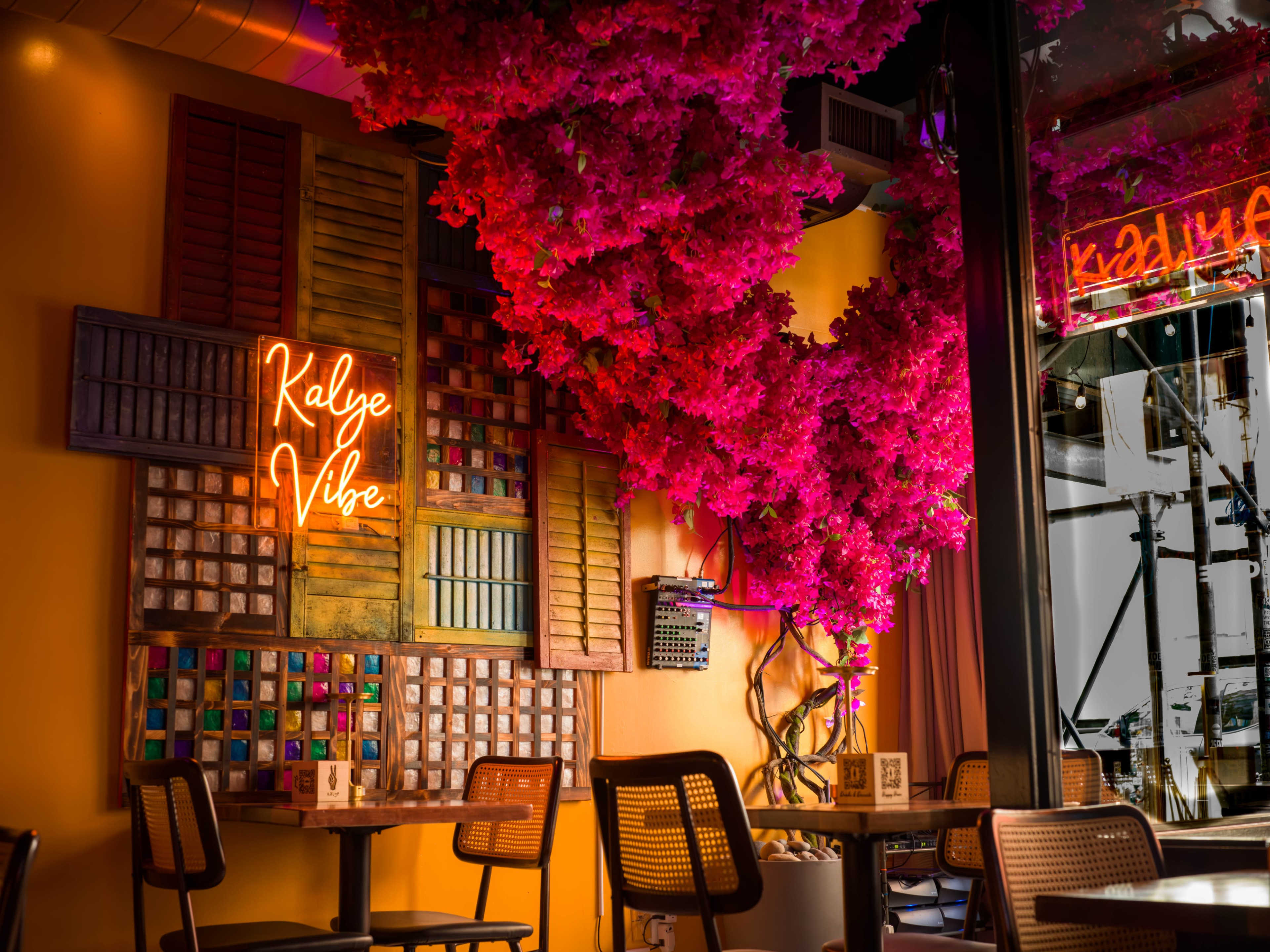 The image depicts a brightly colored restaurant interior adorned with a large artificial tree and a neon sign that reads "Kalye Vibe."