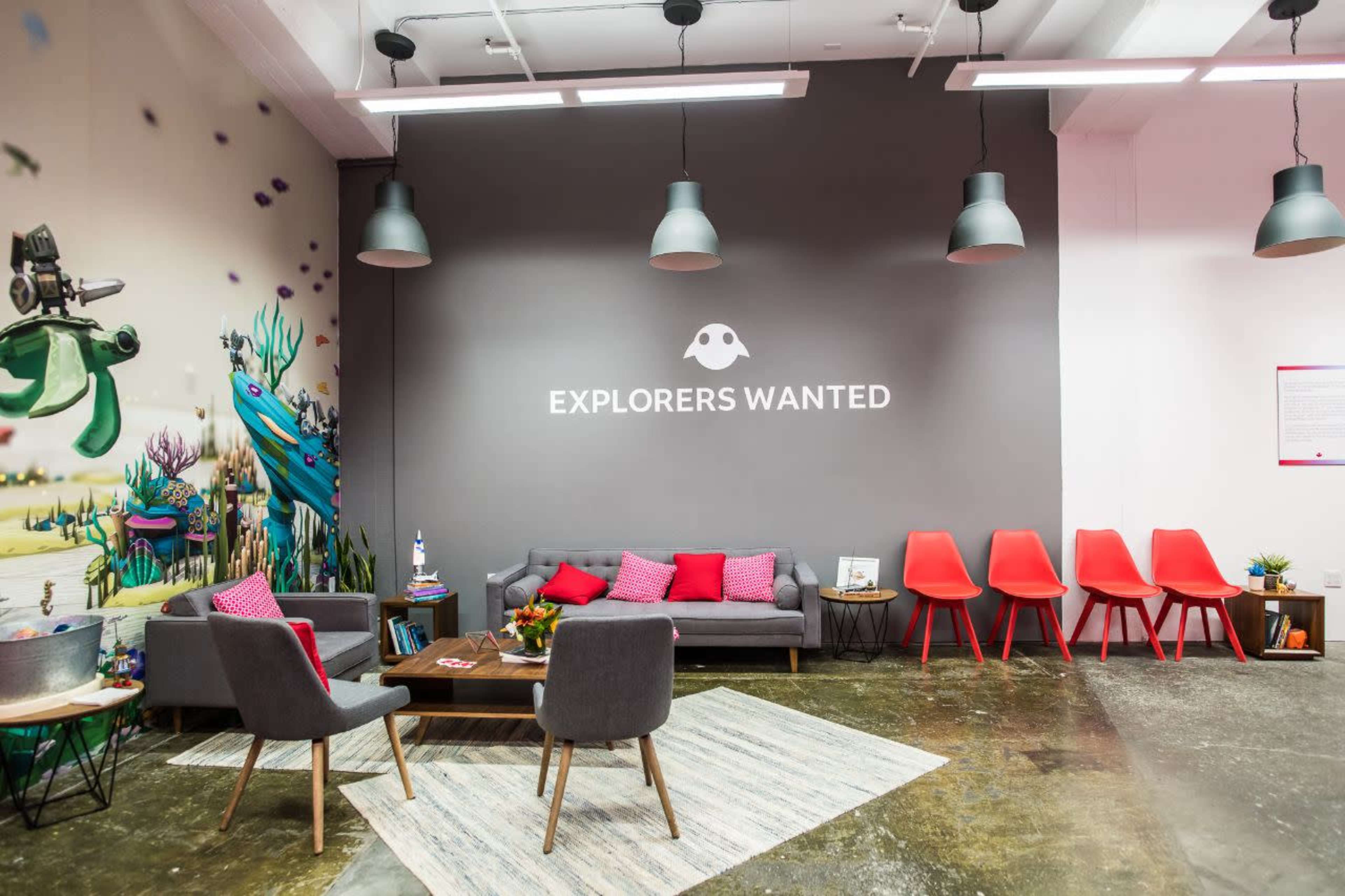 A modern lounge area featuring colorful decorations, a large wall mural with aquatic themes, and a prominent sign that reads "EXPLORERS WANTED."