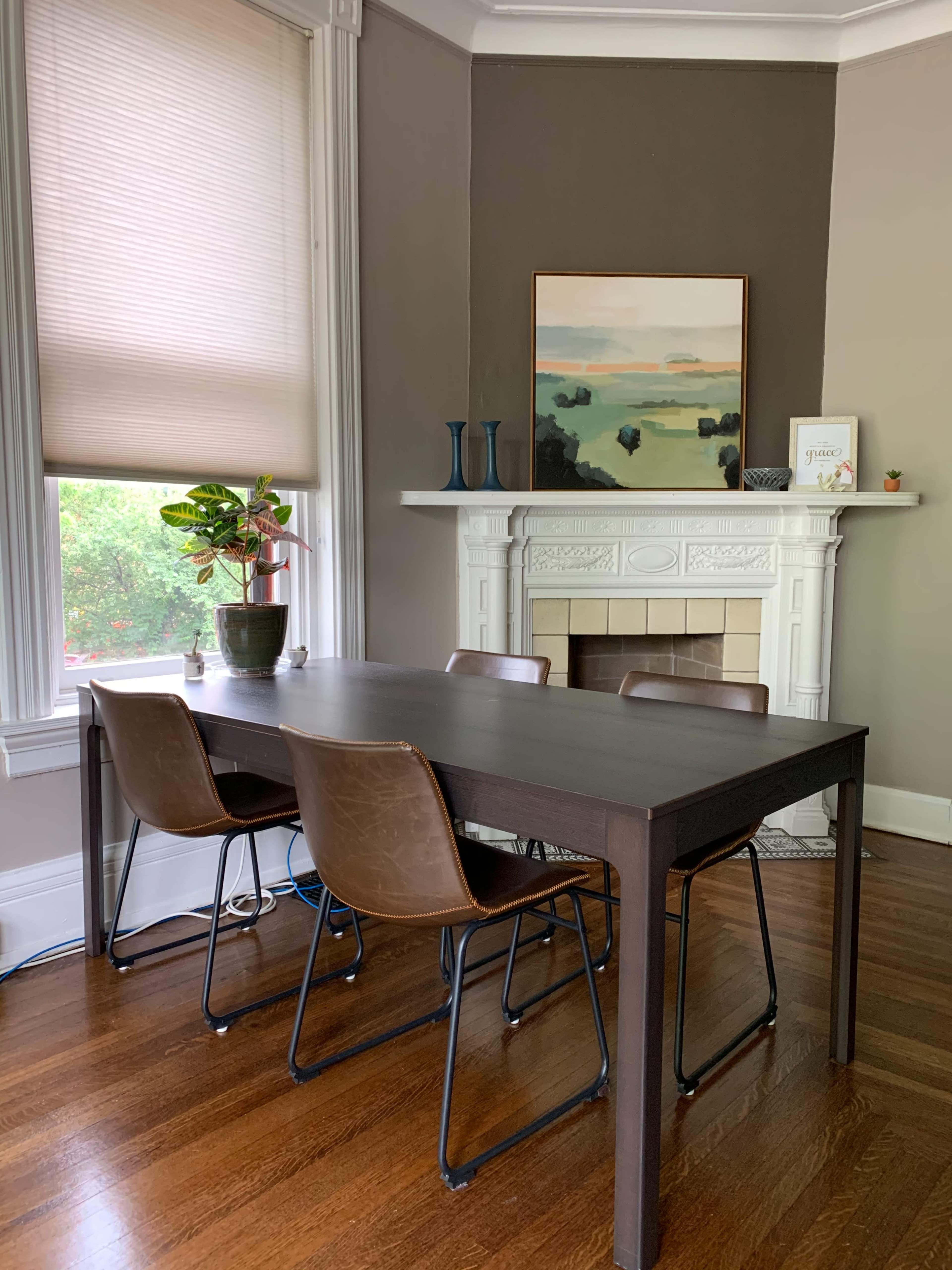 A dining area features a rectangular table with four chairs, a potted plant on the table, and a fireplace adorned with artwork and decorative items.