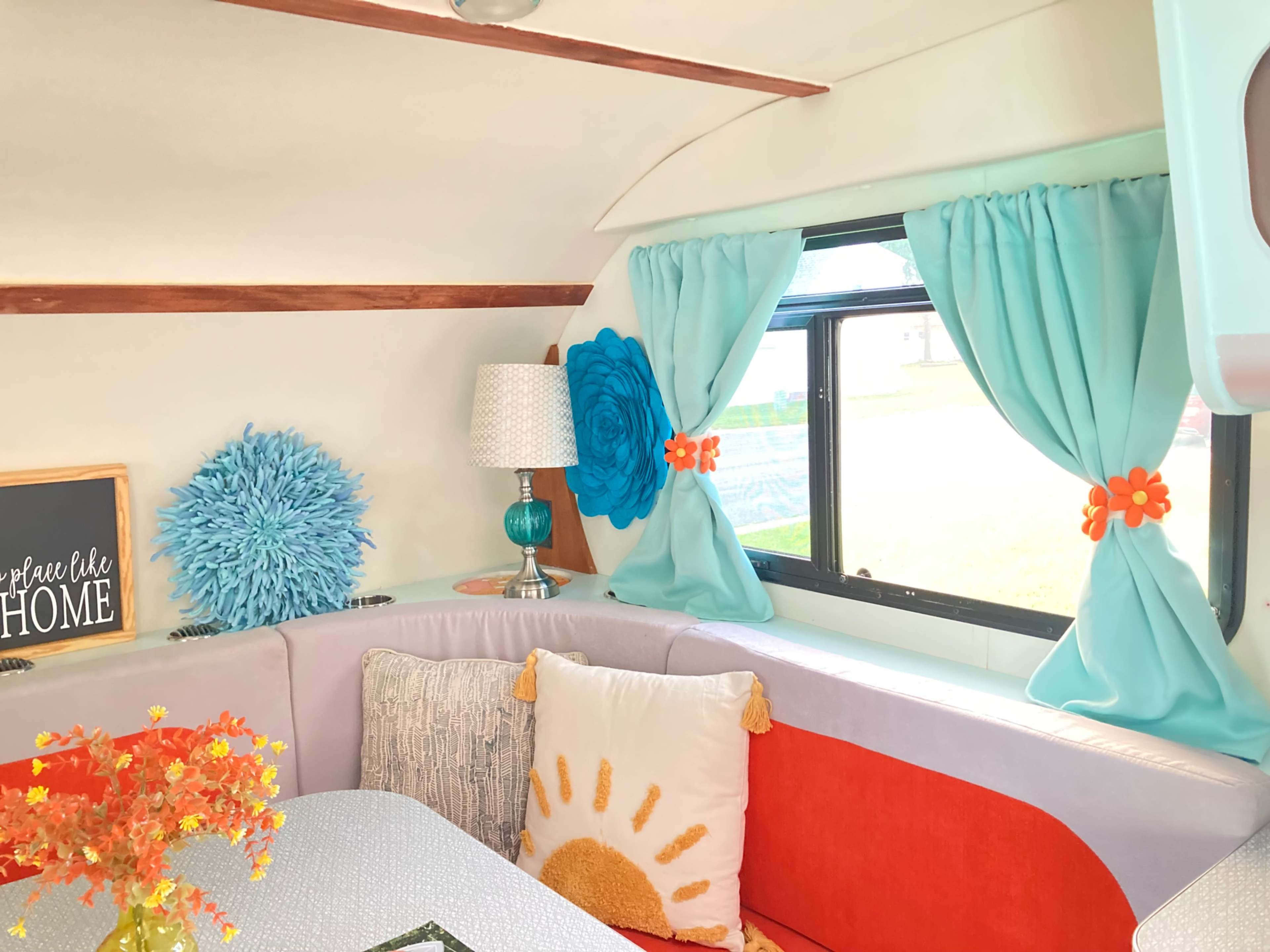 The interior of a colorful camper features a cozy seating area with vibrant pillows, decorative curtains, and a small lamp.