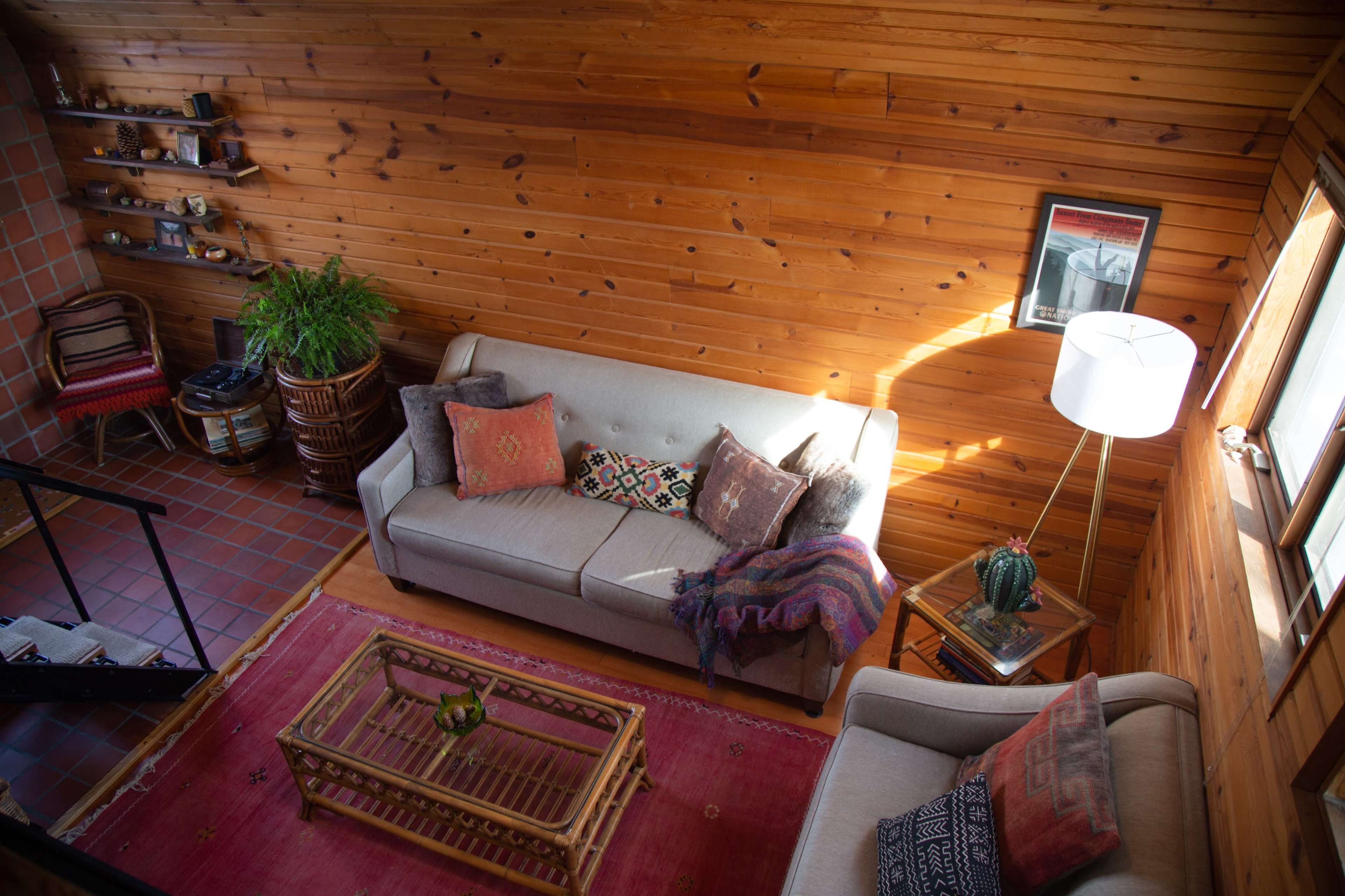 A cozy room with wooden walls, featuring two sofas, a coffee table, a floor lamp, and decorative plants.