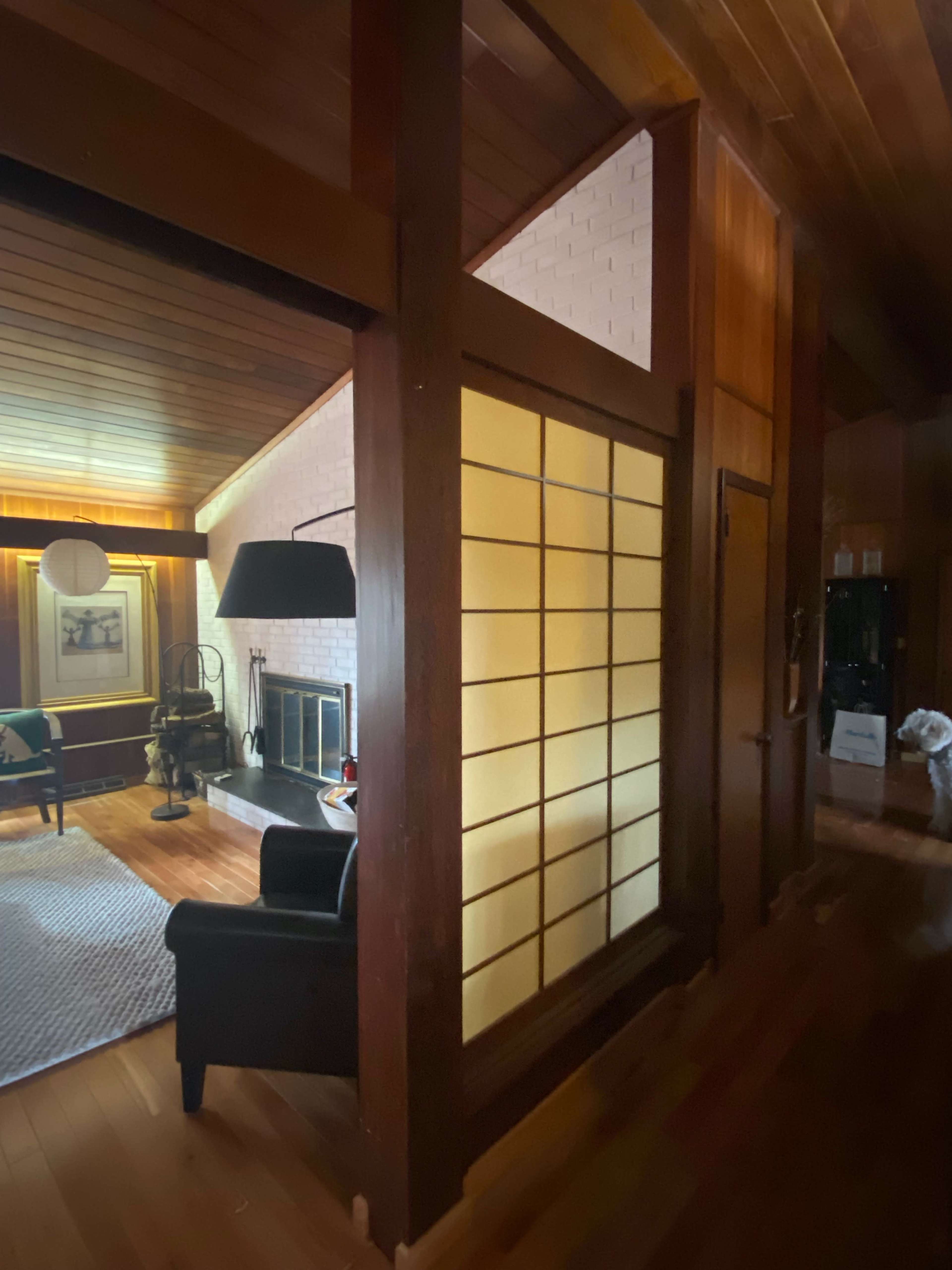 A wooden interior with a view of a room featuring a fireplace, a black armchair, and a partition with shoji-style sliding doors.