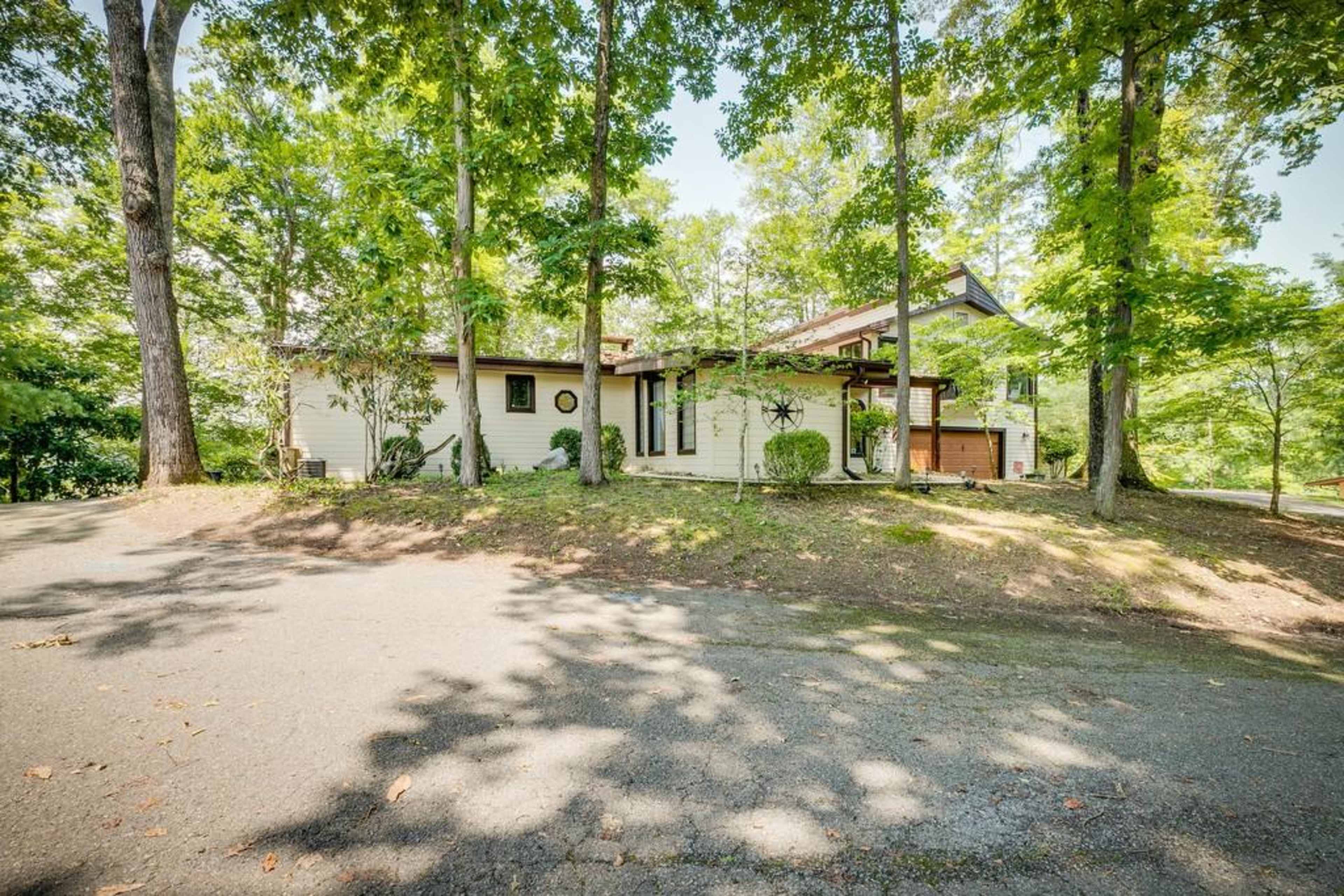 A single-story house is situated among trees, with a driveway leading up to it.