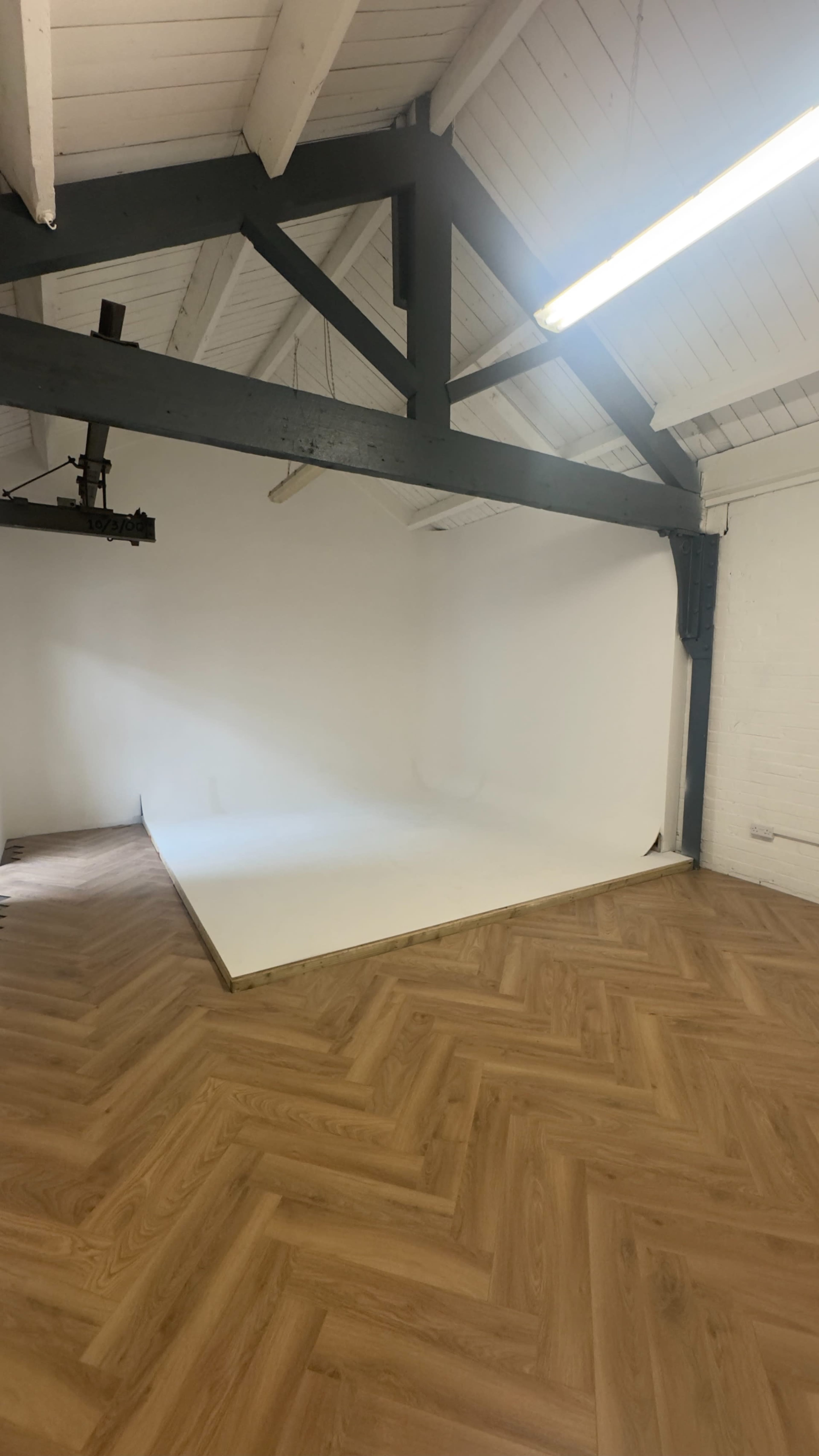 The image shows a spacious studio with a wooden herringbone floor and a white backdrop against a wall.