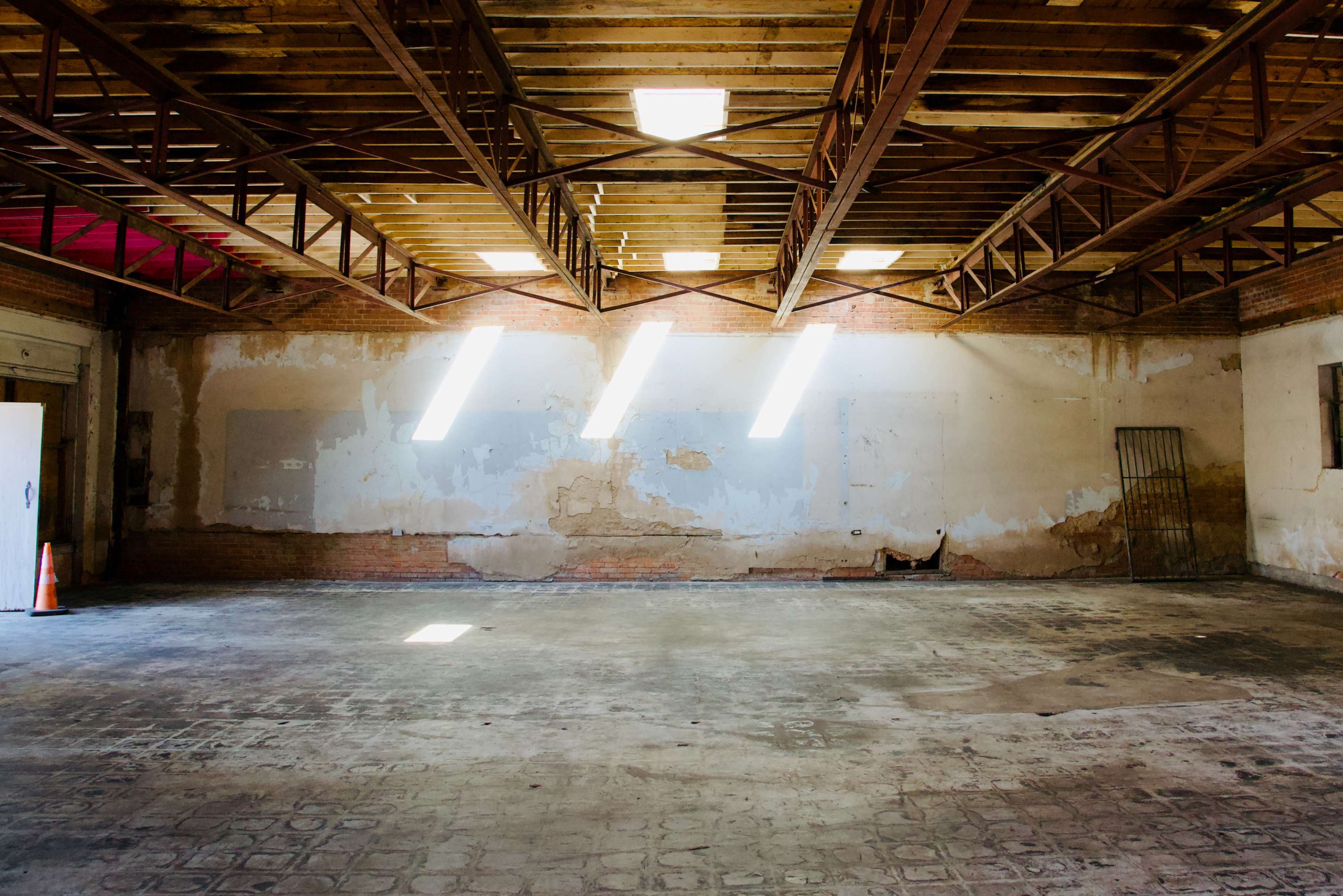 An empty, industrial space with exposed beams and patches of light streaming through the windows onto the concrete floor.