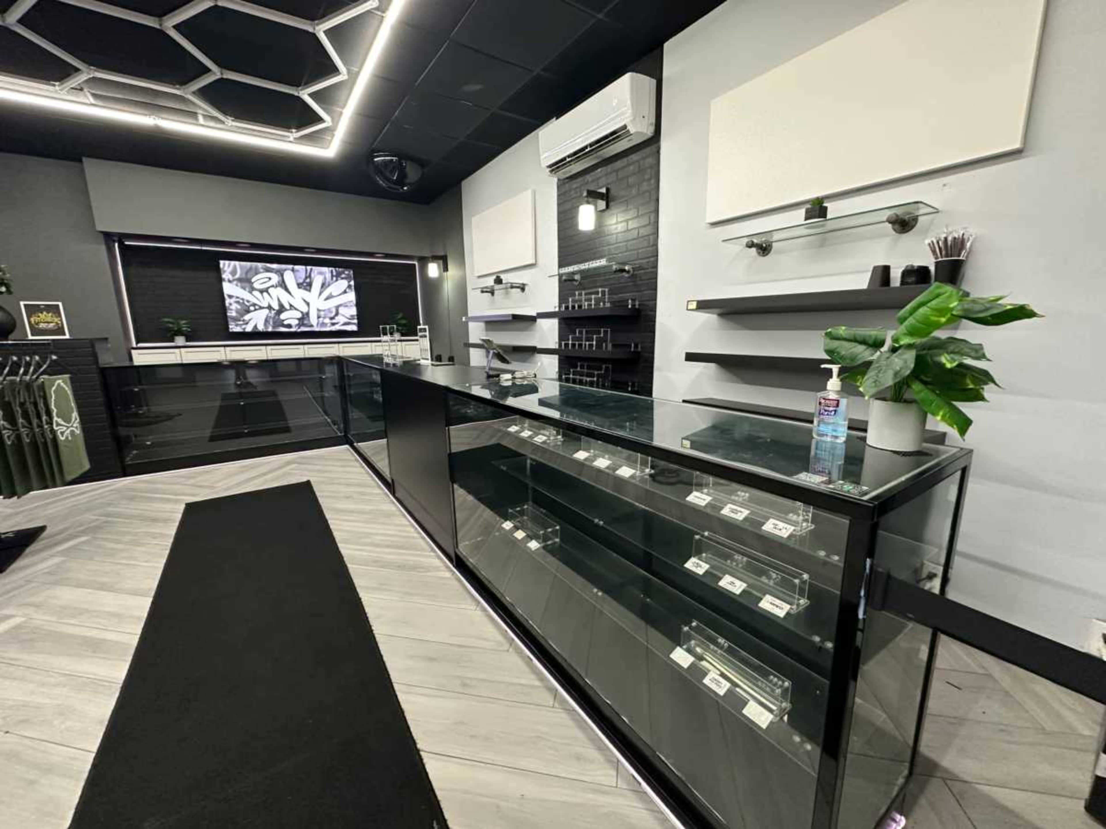 The image shows a modern retail space featuring a sleek glass display counter, minimalist shelving, and a digital screen on the wall.