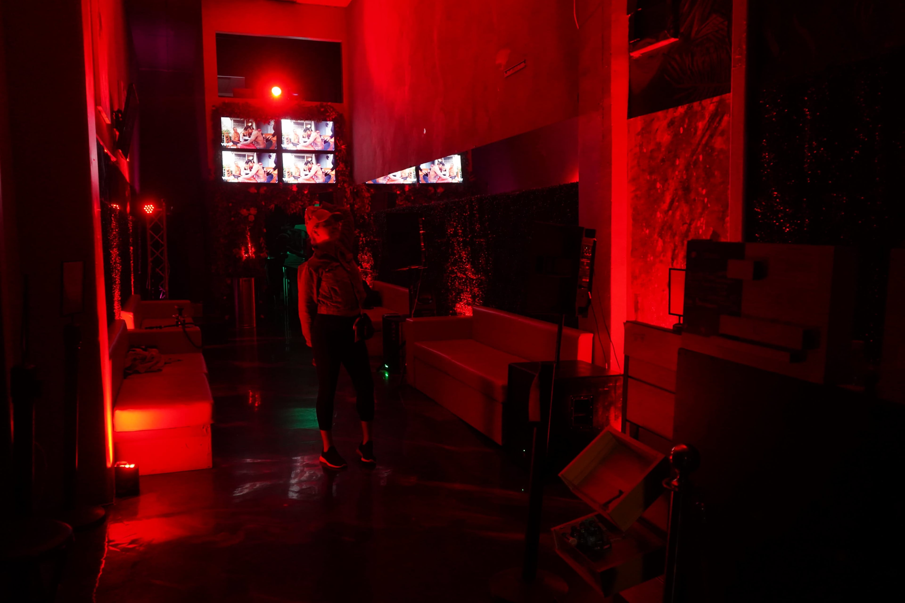 A person stands in a dimly lit room adorned with red lighting and multiple screens displaying images.