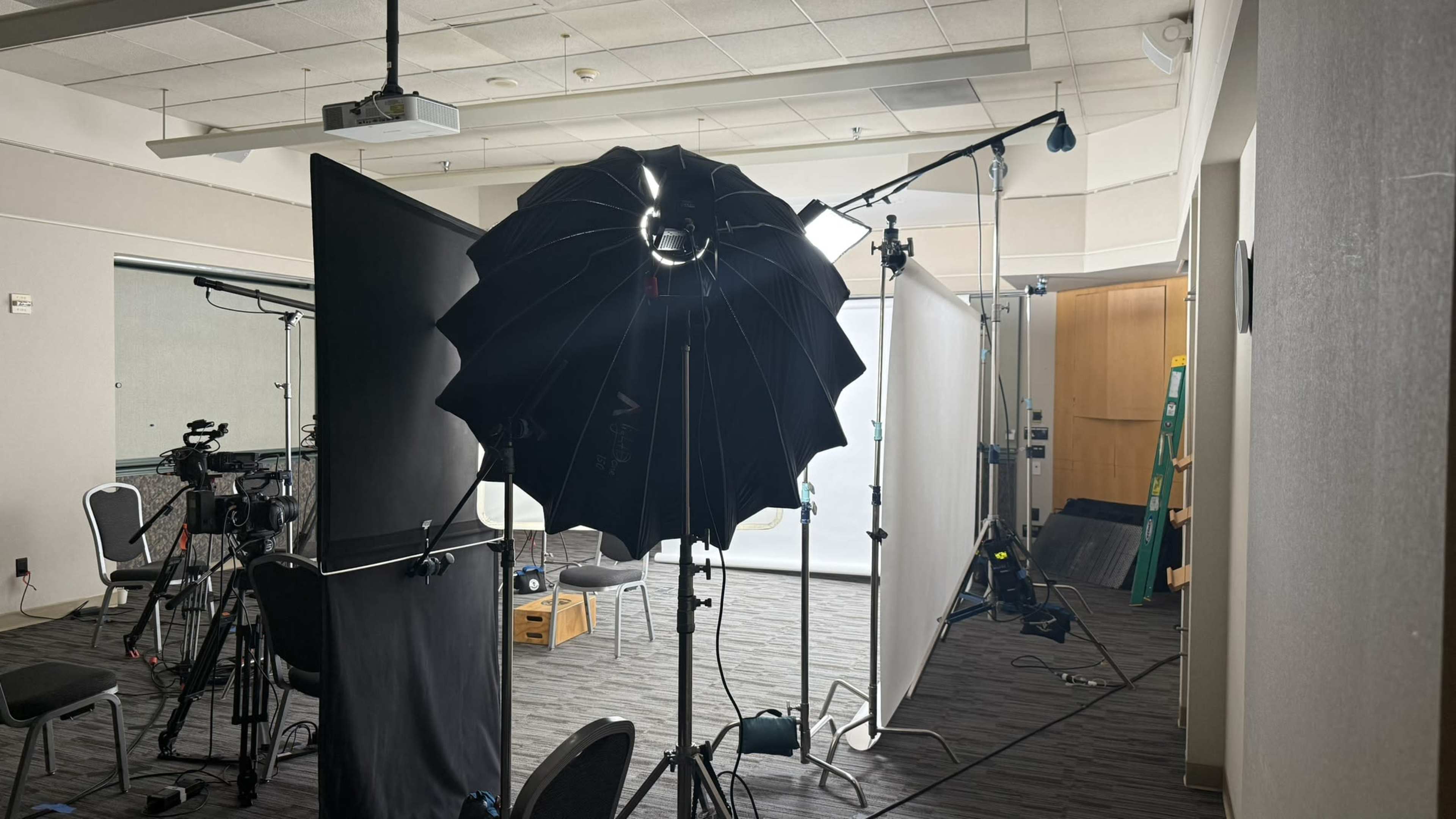 The scene shows a photography setup featuring an umbrella softbox light, a backdrop, and equipment typically used for a studio shoot.
