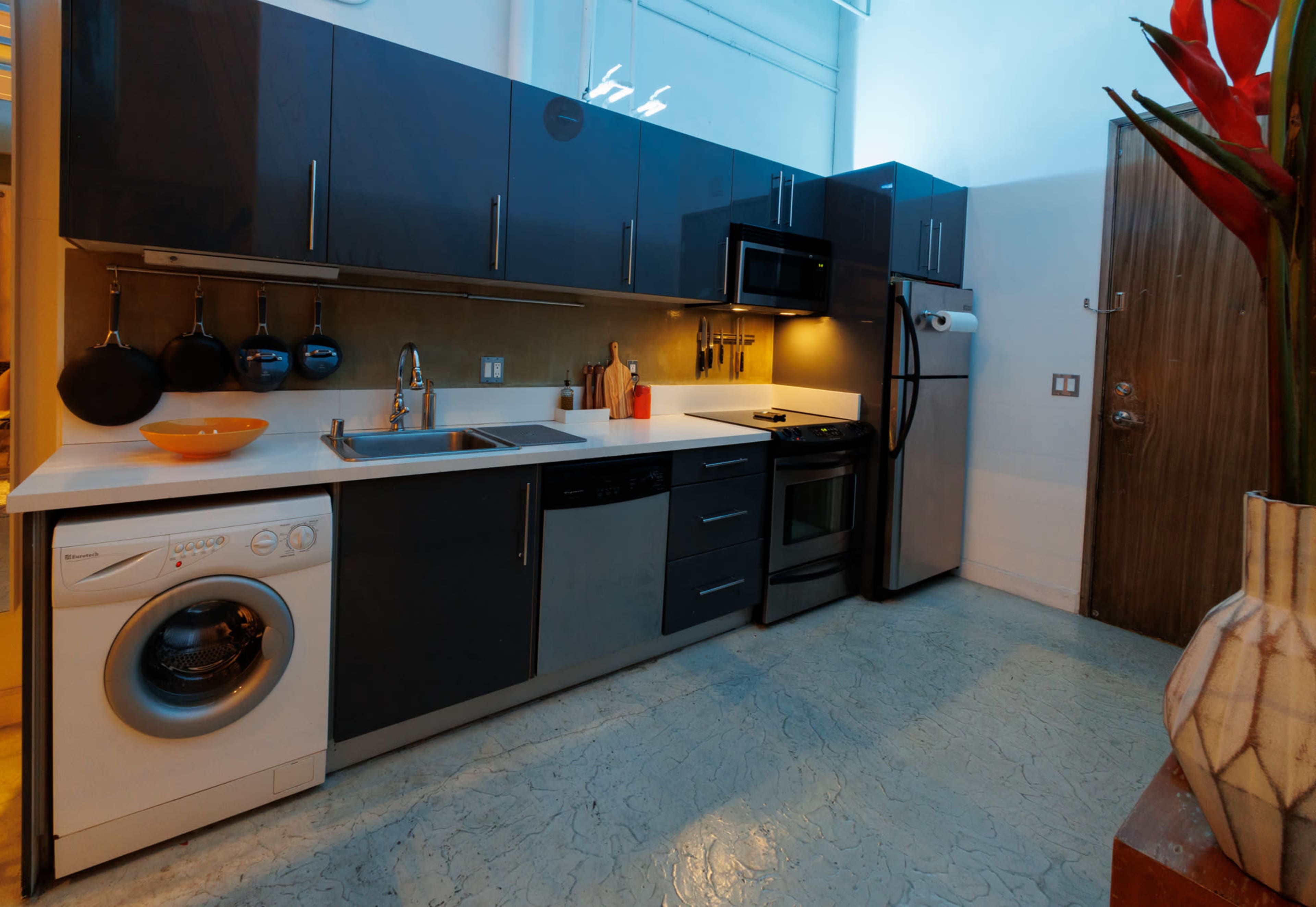 A modern kitchen features dark cabinets, stainless steel appliances, and a washing machine integrated into the design.