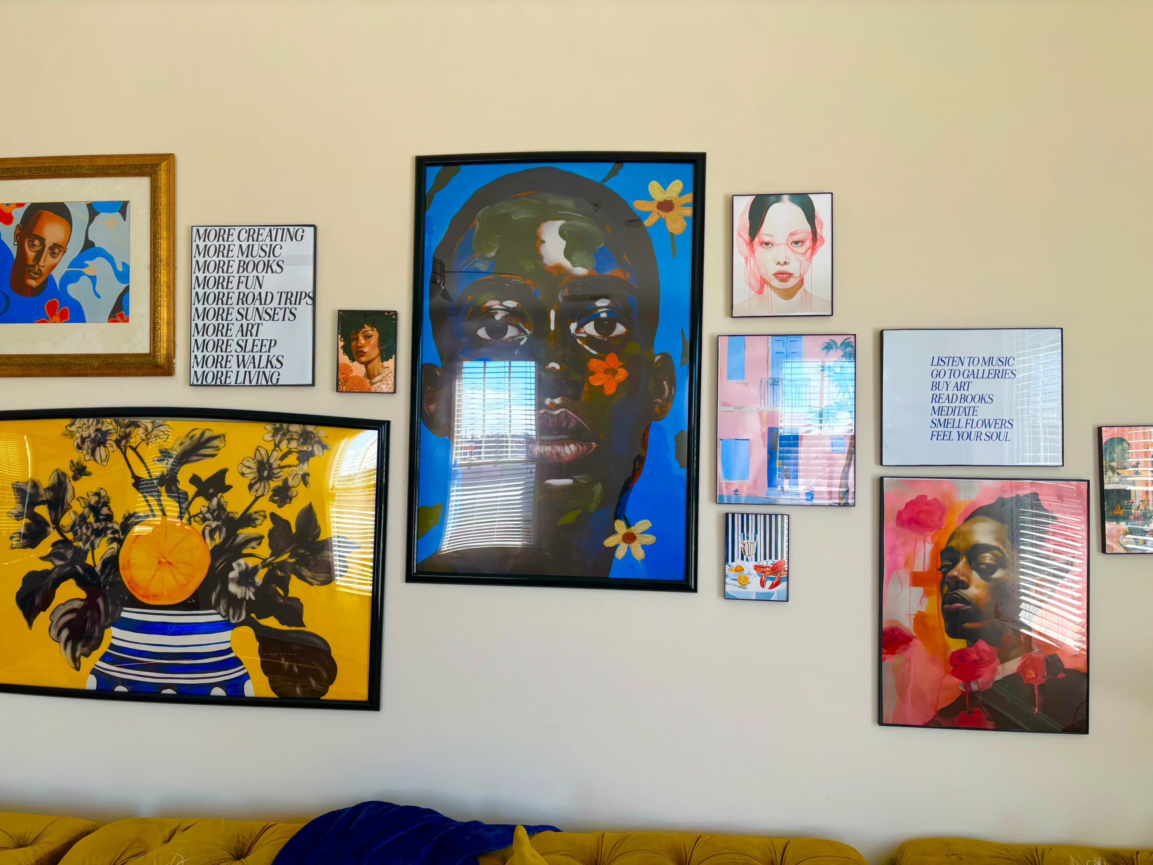 A wall adorned with various framed artworks, including portraits and colorful prints, above a yellow sofa.