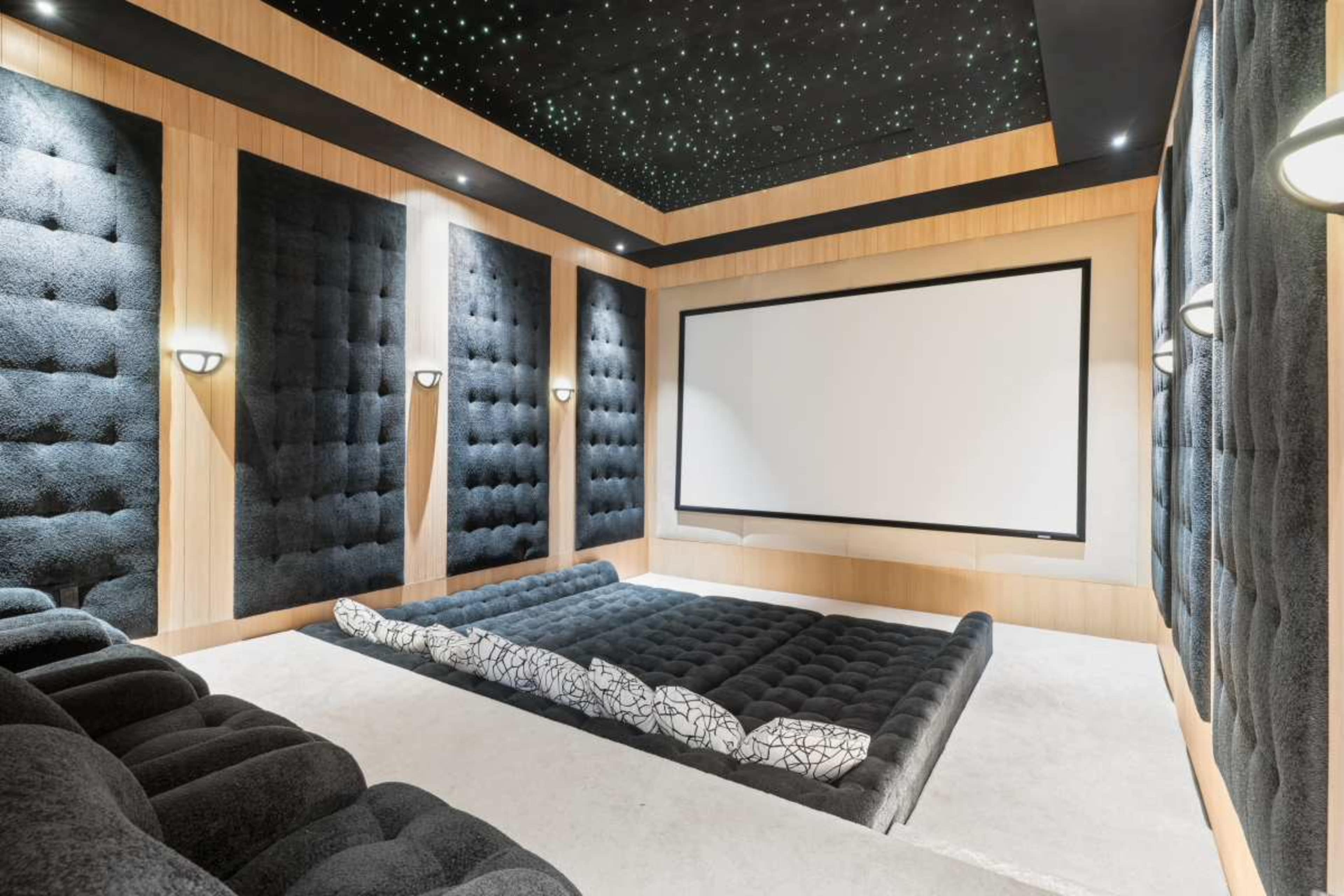 The image shows a modern home theater with plush dark seating, a large blank projection screen, and a starry ceiling.