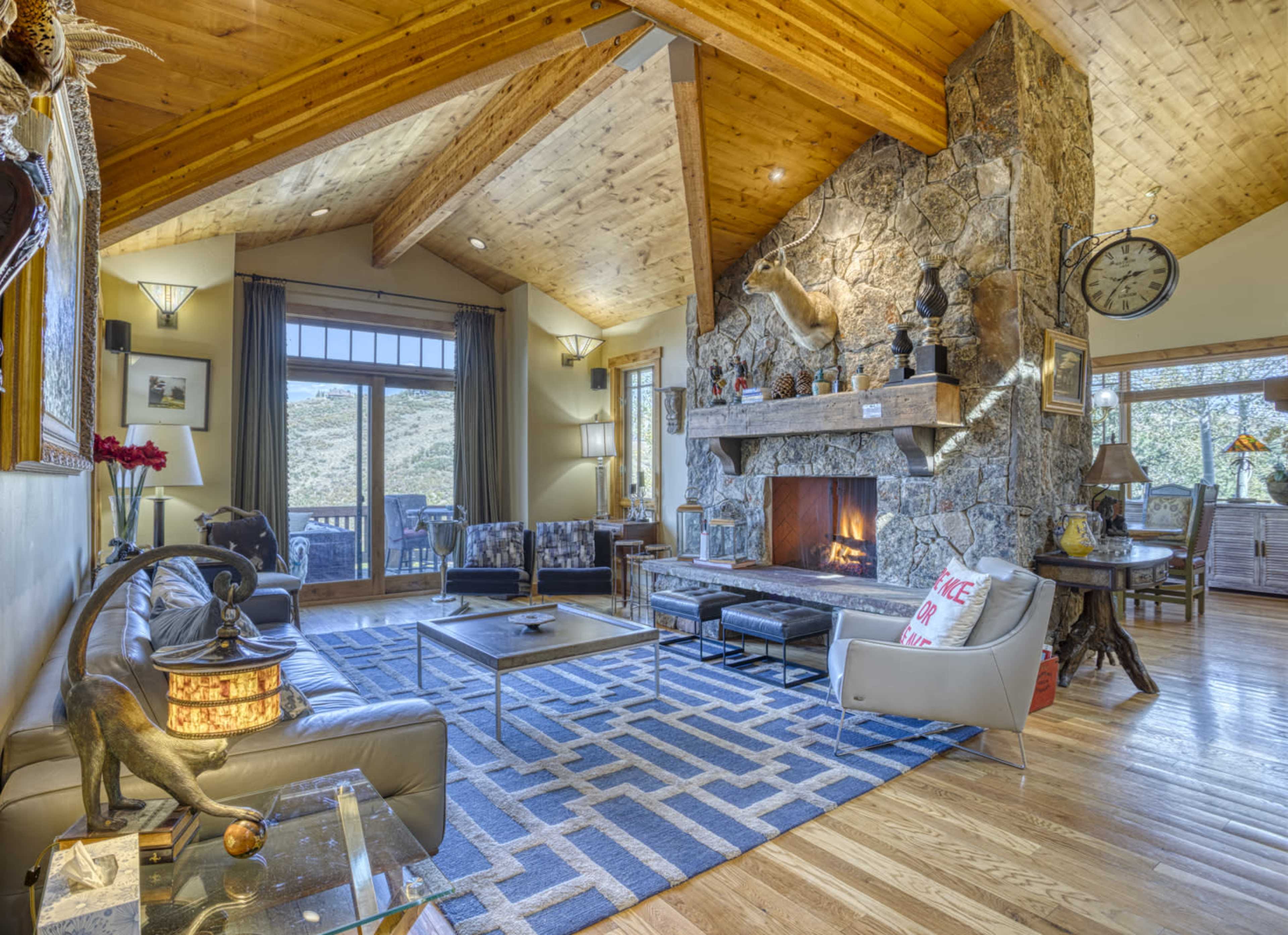 The living room features a stone fireplace, large windows with a view, and a mix of modern and rustic furnishings.