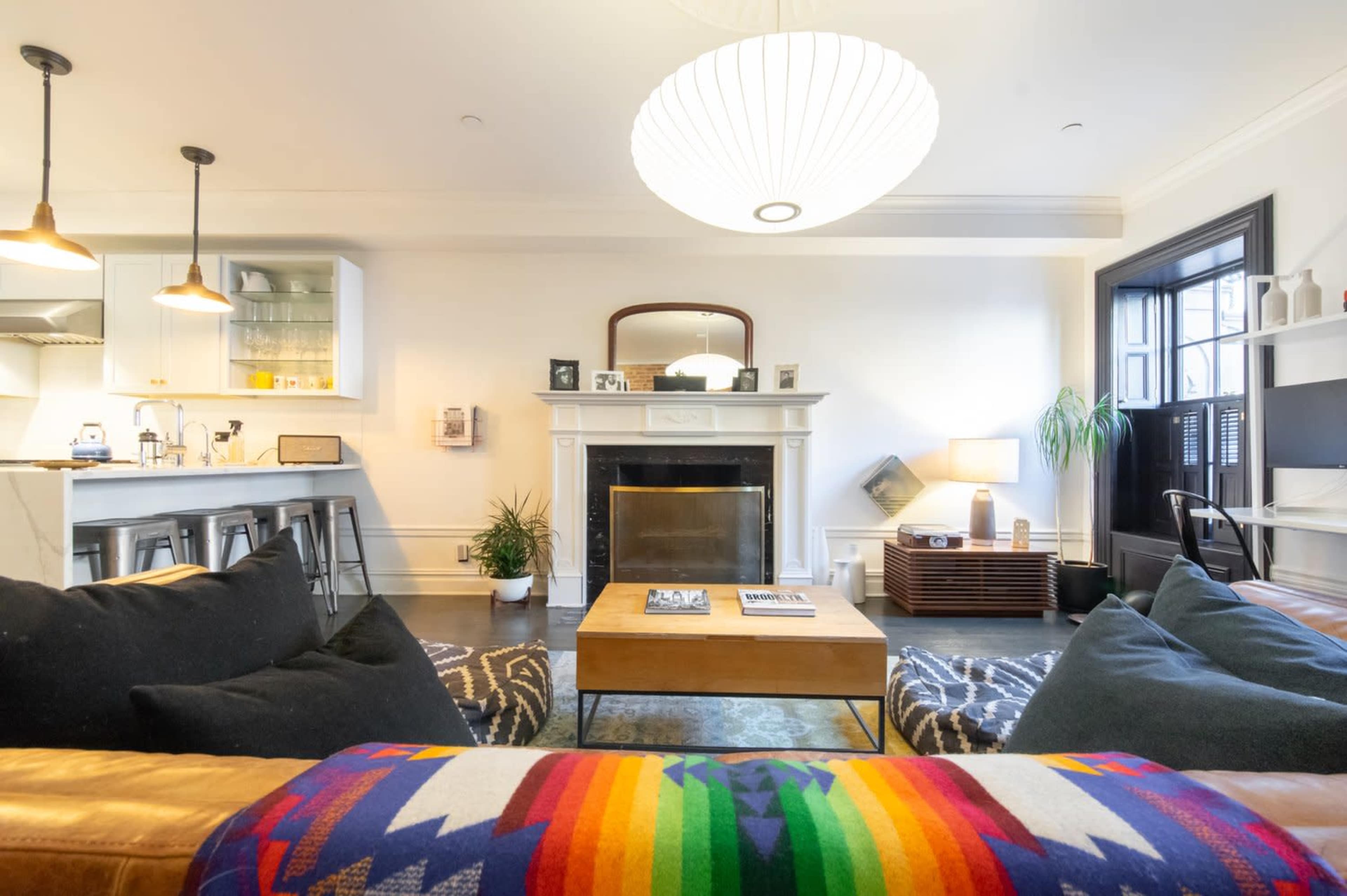 The living room features a large brown leather sofa, a wooden coffee table, and a fireplace with a mirror above it, surrounded by white walls and modern decor.