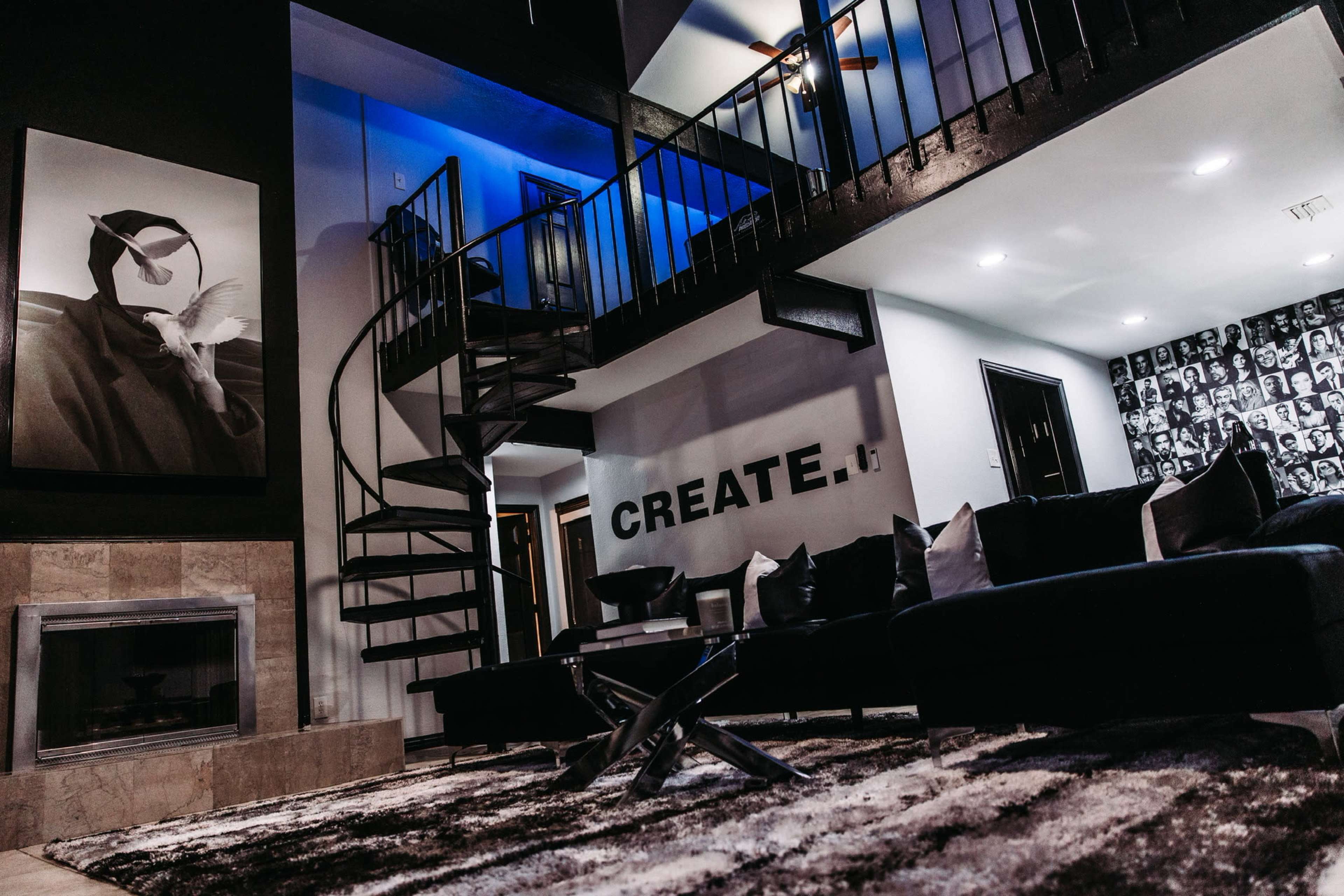 A modern interior featuring a spiral staircase, a large black-and-white artwork on the wall, and a living area with dark furniture and a patterned backdrop.