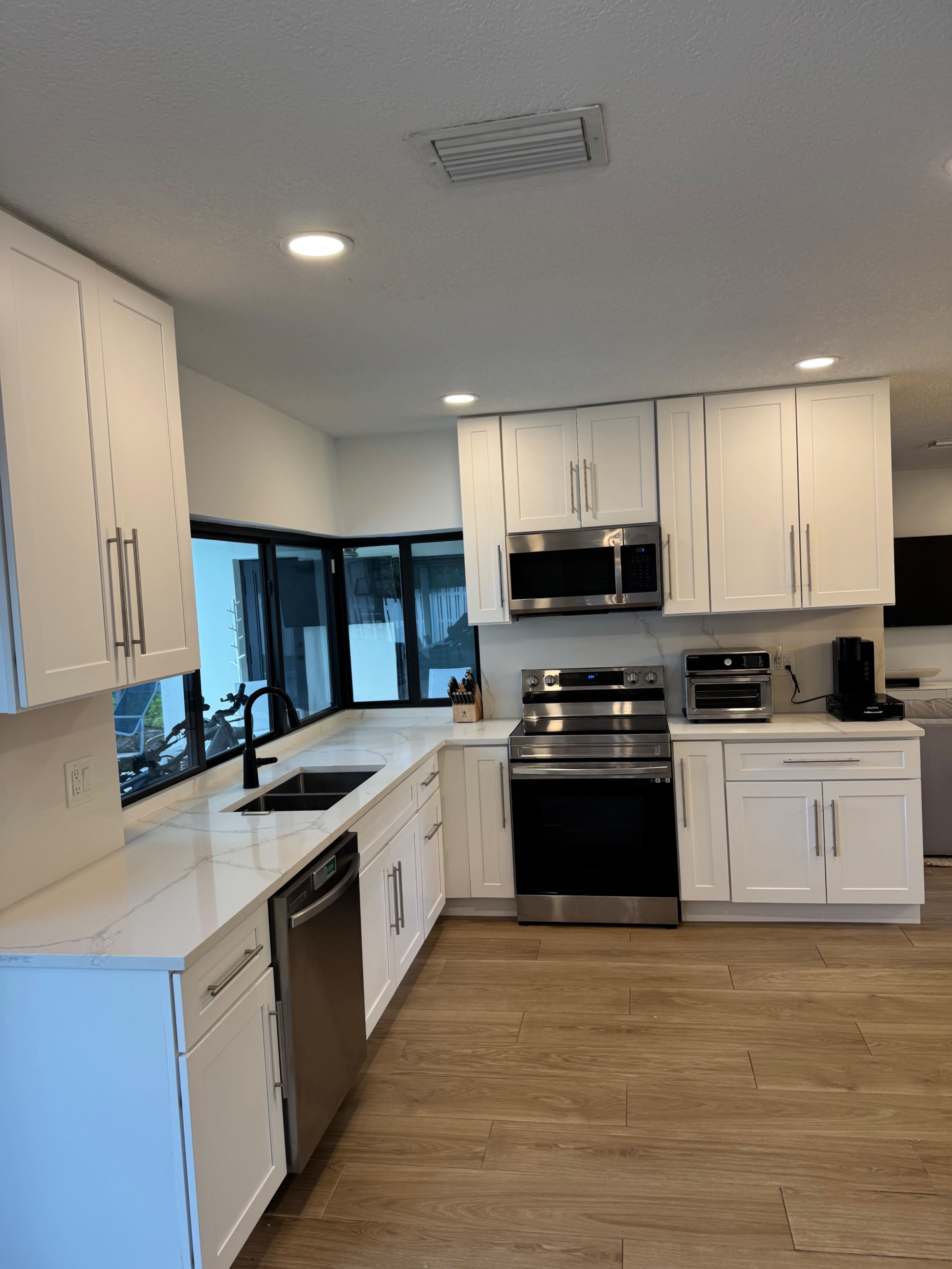 The image shows a modern kitchen with white cabinetry, stainless steel appliances, and a light-colored countertop.