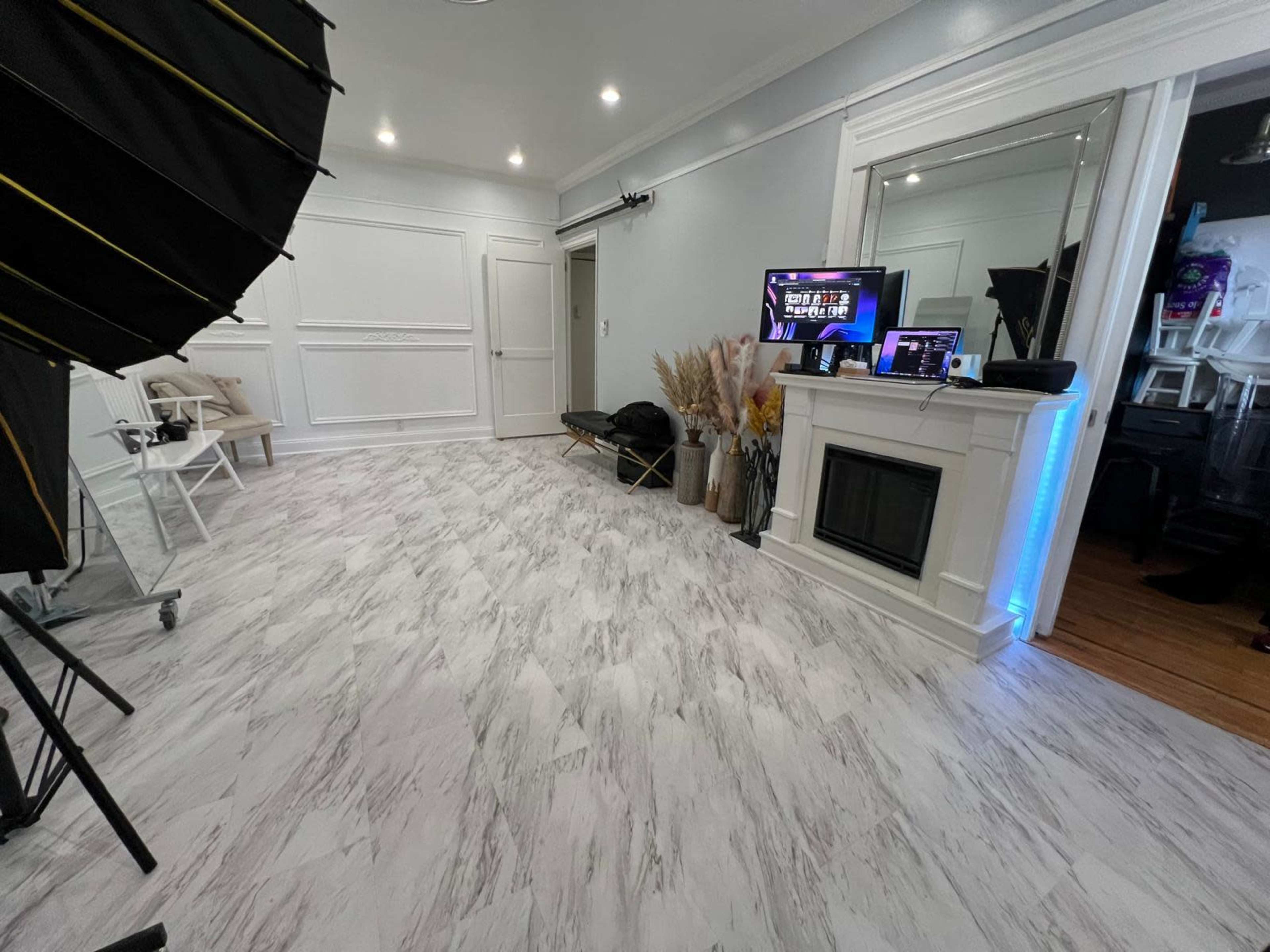 The image shows a well-lit room with a marble-patterned floor, a decorative fireplace, a large mirror, and photography equipment on one side.