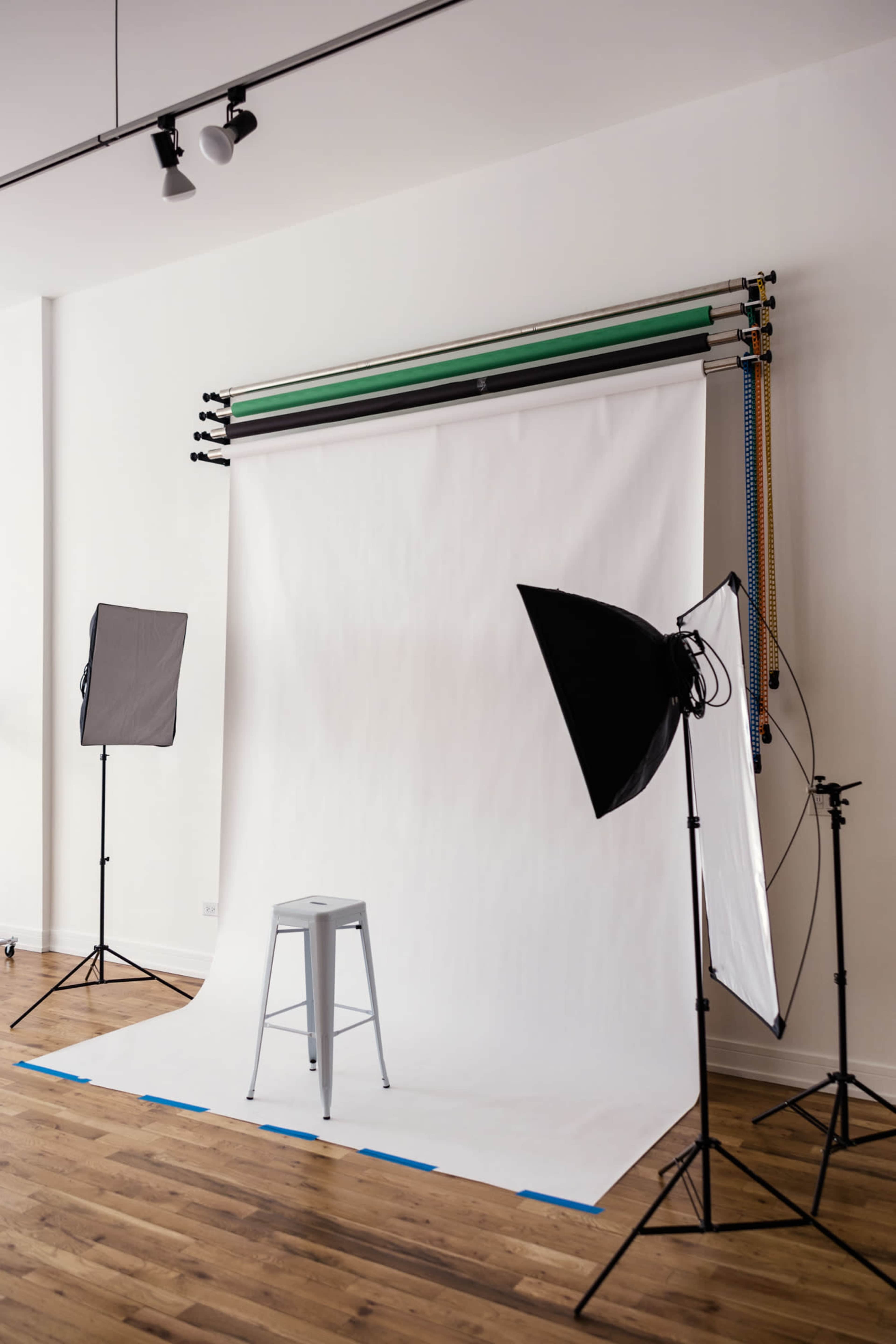 A photography setup featuring a white backdrop, a stool, and multiple studio lights arranged around the scene.