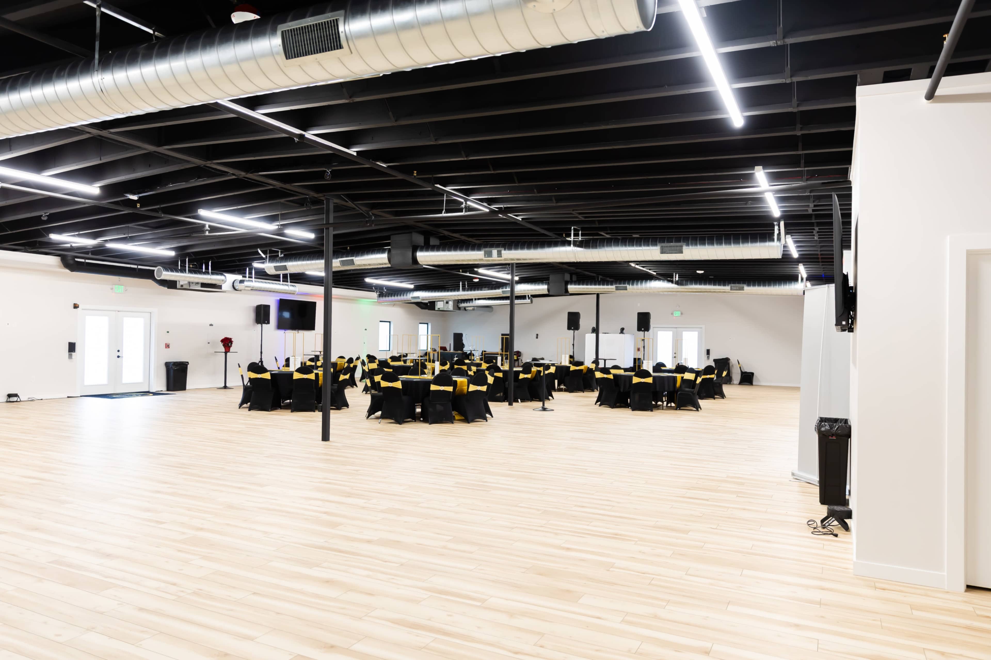 The image shows a spacious event hall with several round tables covered in black tablecloths adorned with yellow accents.