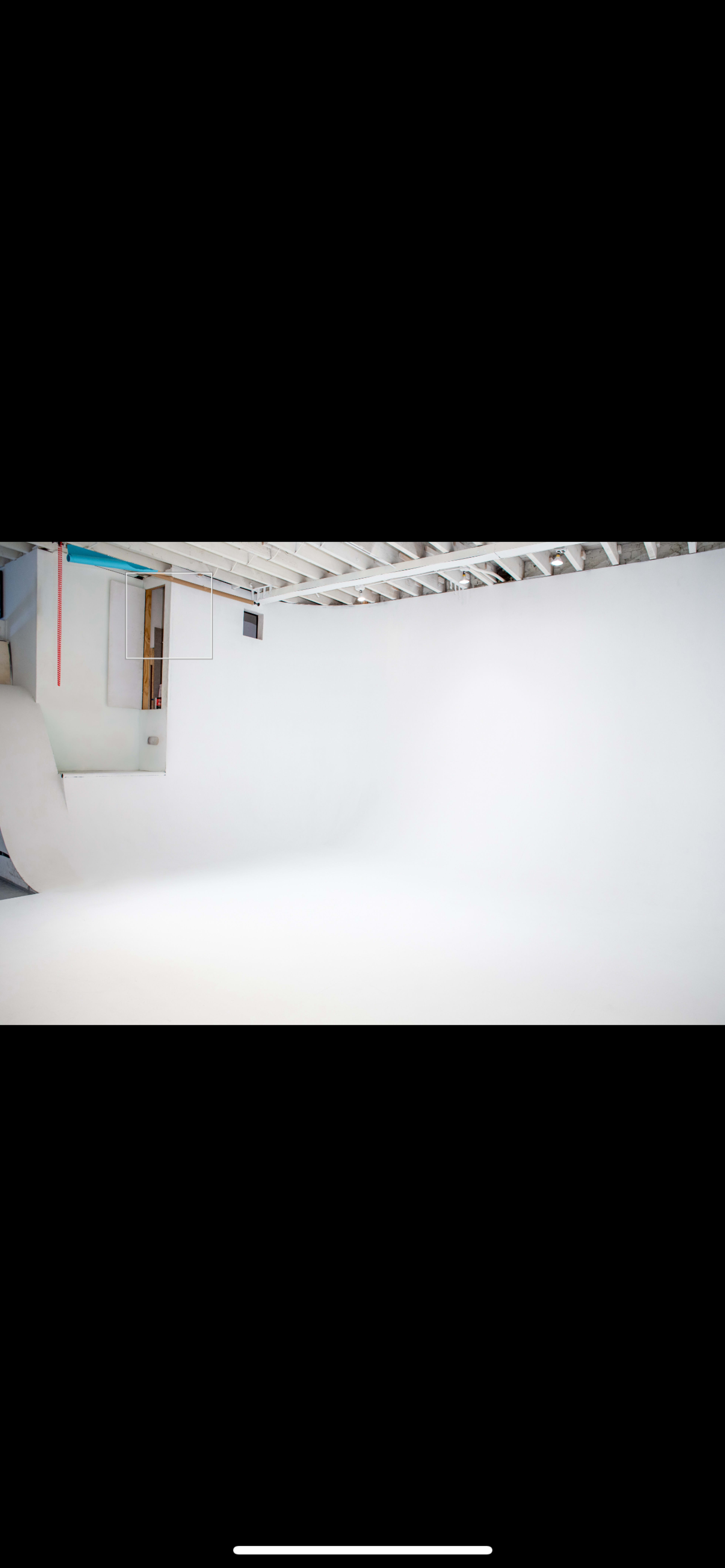 The image shows a spacious photography studio with a seamless white background and minimal equipment.