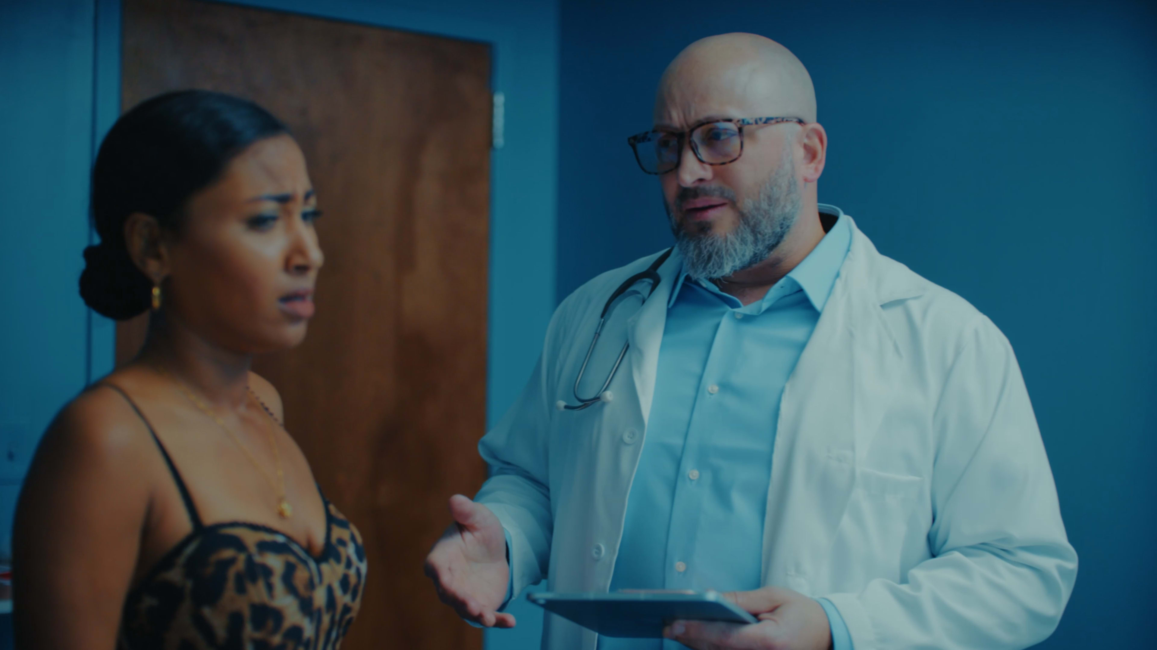 A doctor in a white coat speaks with a woman in a leopard-print top in a medical office.